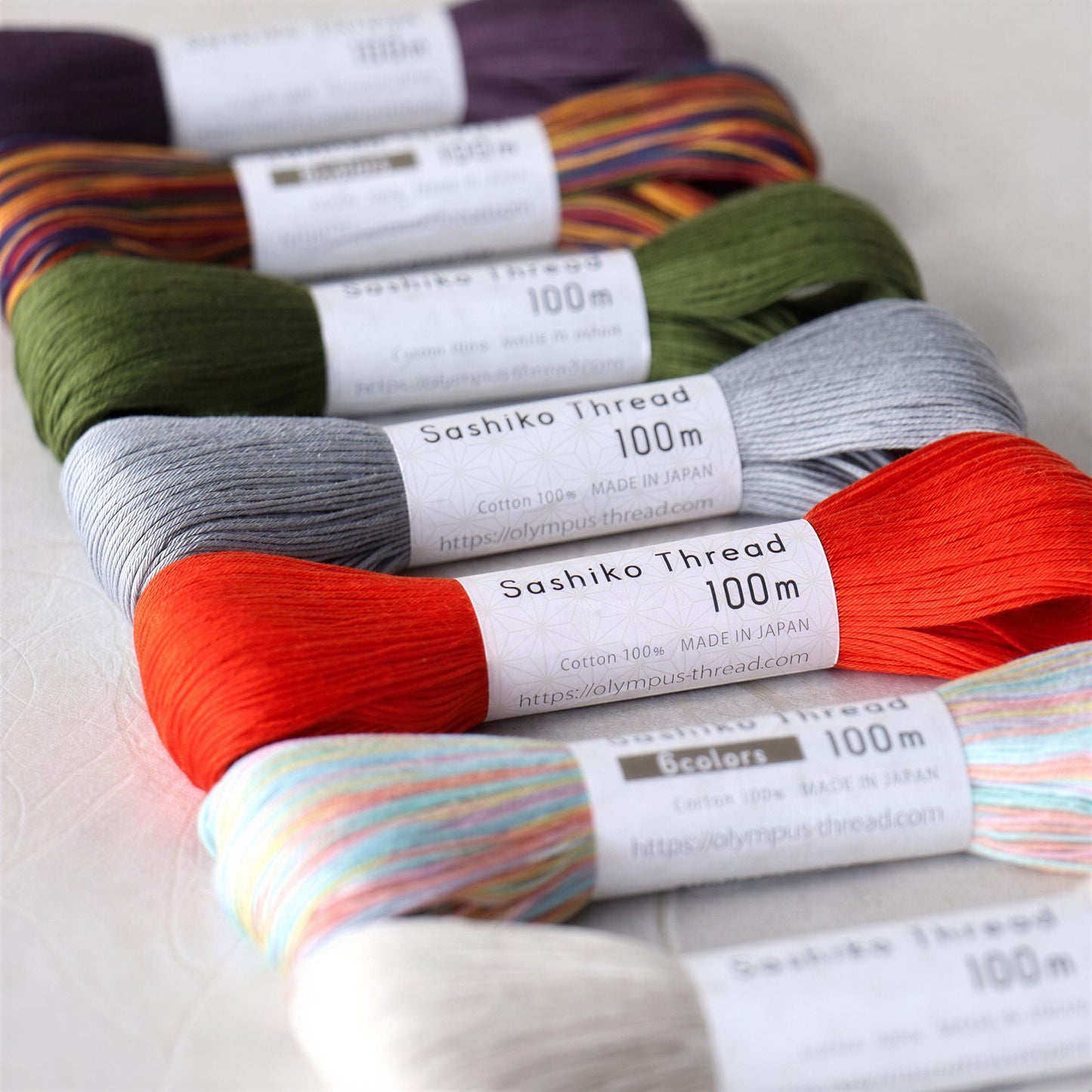 A row of colorful spools of thread, each labeled with the brand name "Sashiko Thread" and the size "100m".