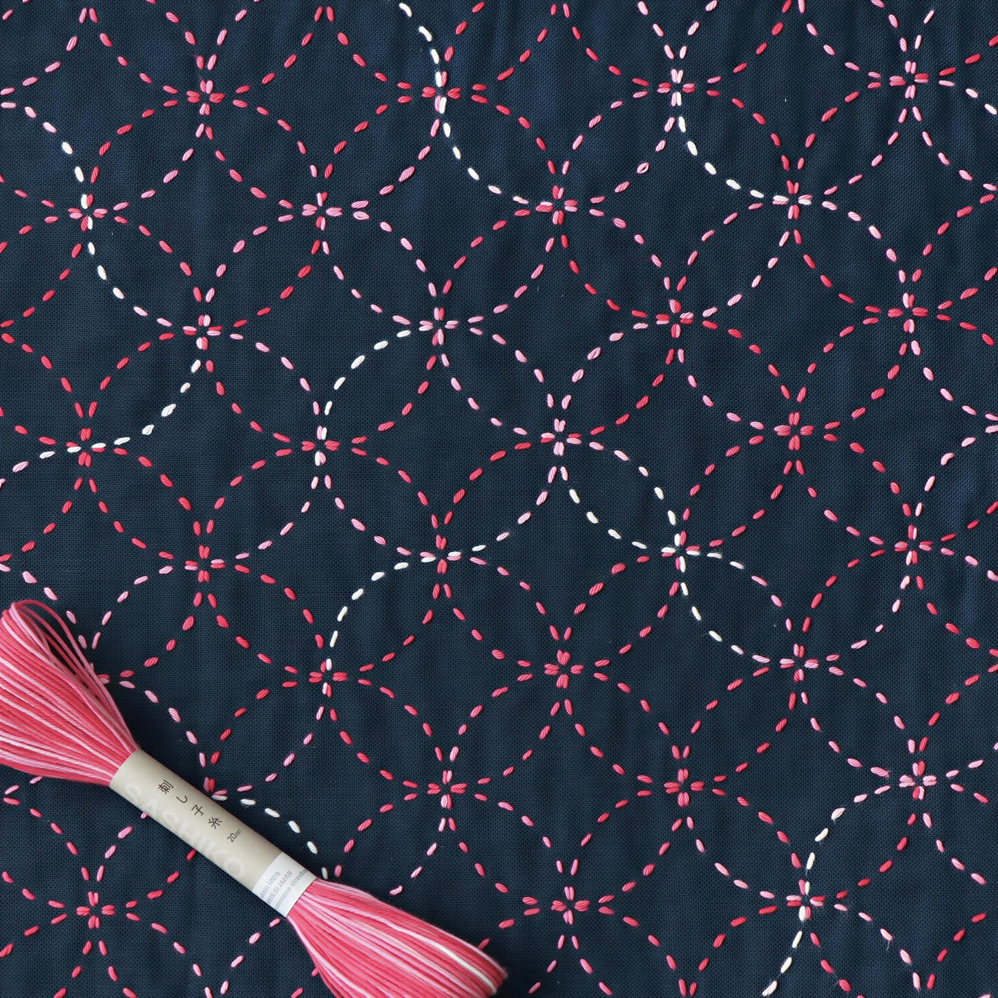 a close-up view of a fabric with a repeating pattern of red and white circles, creating a visually striking and intricate design. The fabric appears to be dark blue, providing a strong contrast to the vibrant colors of the circles. A spool of thread is also visible in the image, suggesting that the pattern may be used for sewing or embroidery purposes.