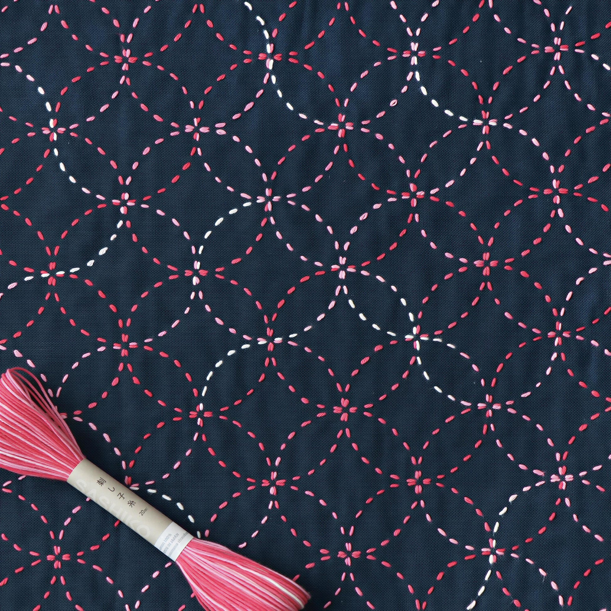 a close-up view of a fabric with a repeating pattern of red and white circles, creating a visually striking and intricate design. The fabric appears to be dark blue, providing a strong contrast to the vibrant colors of the circles. A spool of thread is also visible in the image, suggesting that the pattern may be used for sewing or embroidery purposes.