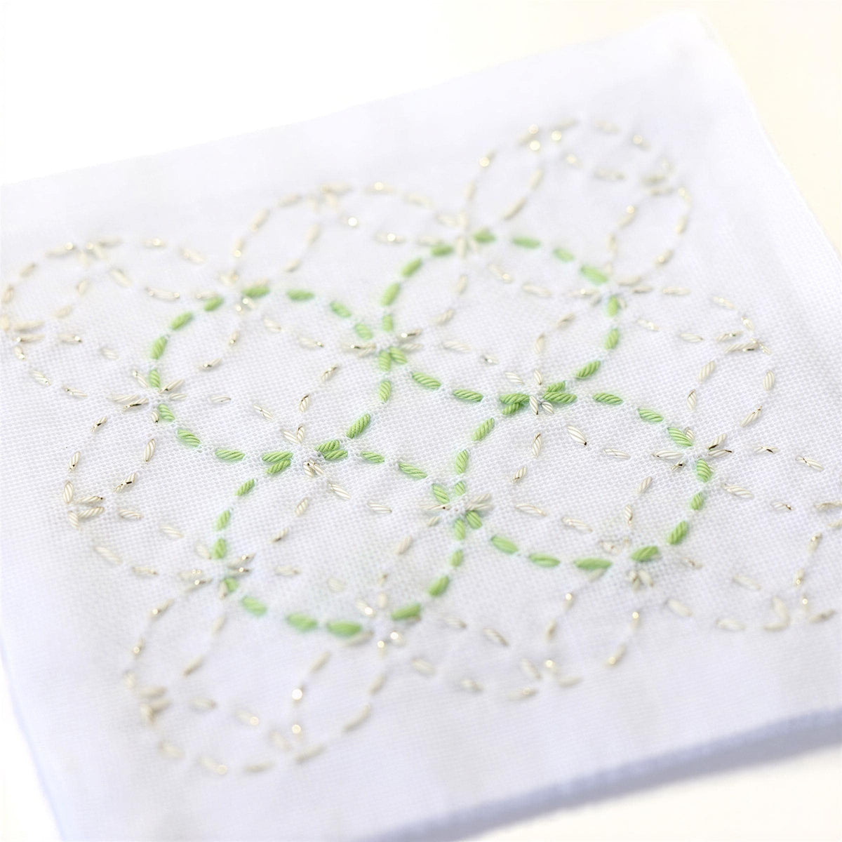 a close-up view of a white fabric with a delicate, intricate embroidered design featuring green and white flowers or leaves.