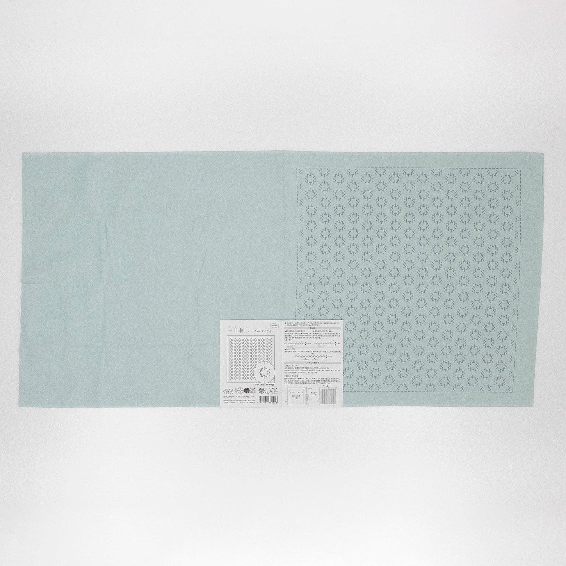 The image is a light blue fabric with a pattern of small white dots or circles on it, and there is a small white label or piece of paper with text and a barcode attached to it.
