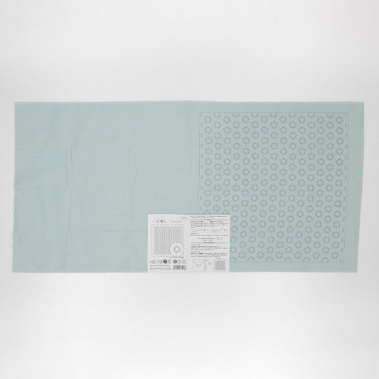 The image is a light blue fabric with a pattern of small white dots or circles on it, and there is a small white label or piece of paper with text and a barcode attached to it.
