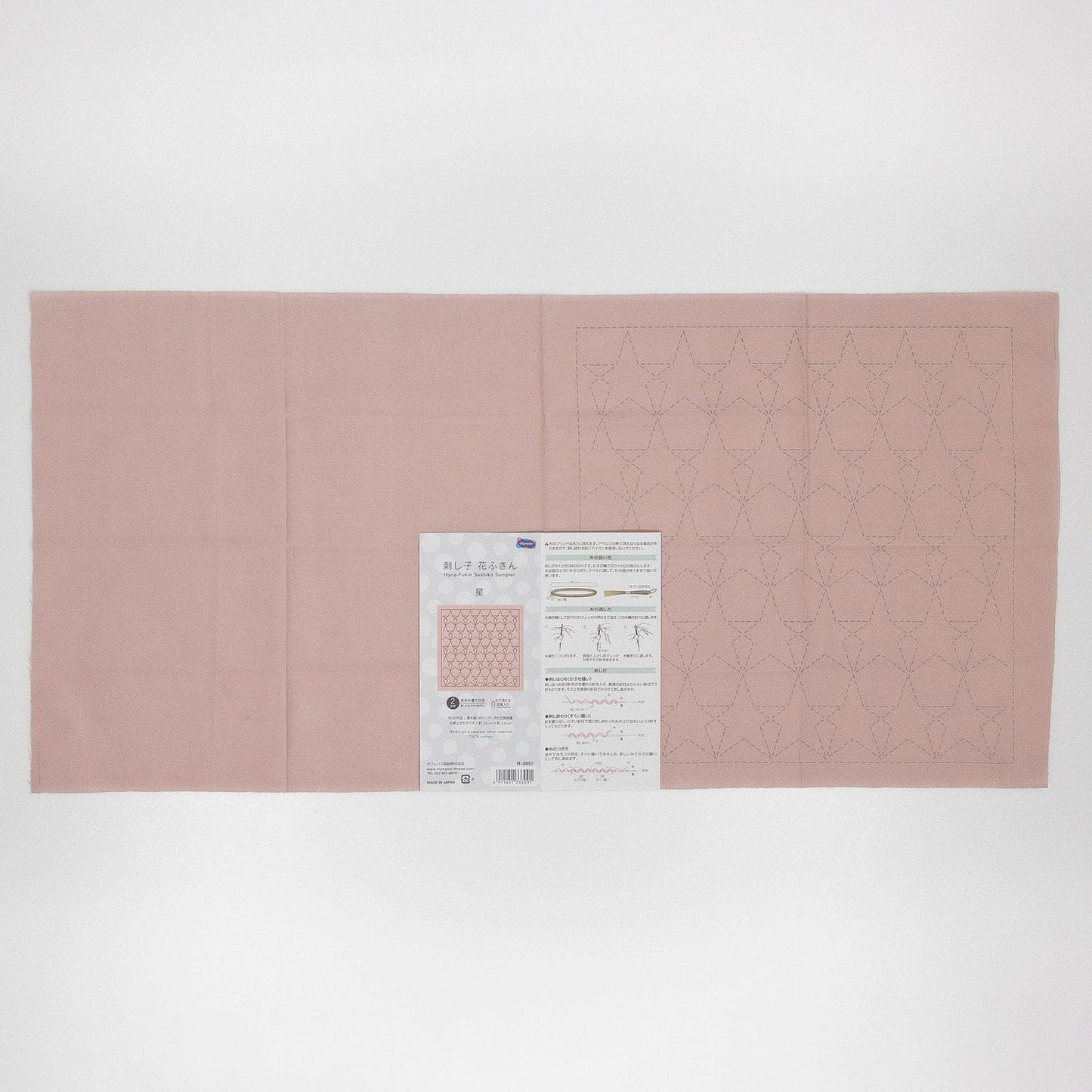 The image is a pink fabric with a pattern of small white dots or lines, and there is a printed paper with instructions or information about the fabric.