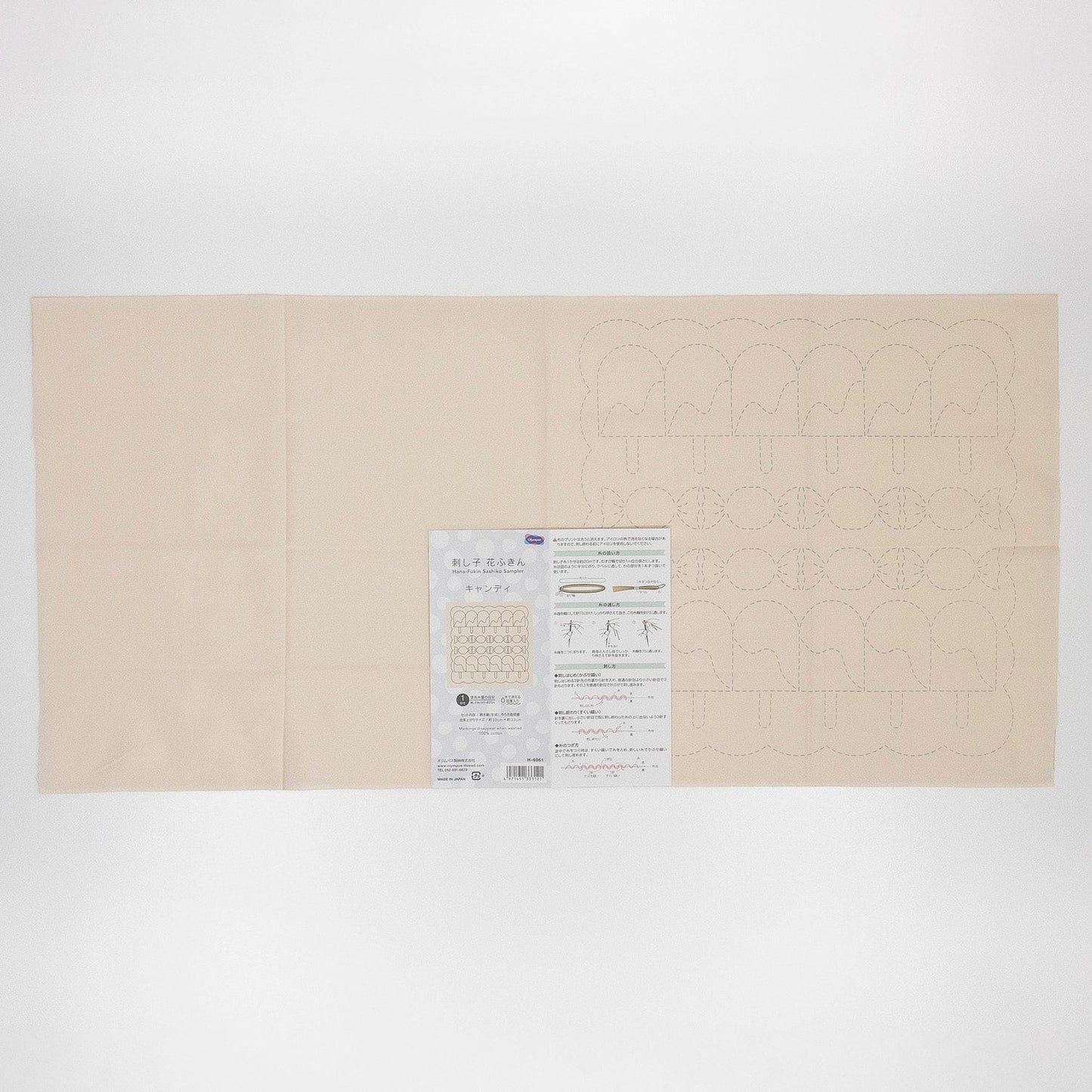 The image is a large, cream-colored fabric with a printed pattern on it. There is a small, white paper with text and diagrams next to the fabric.