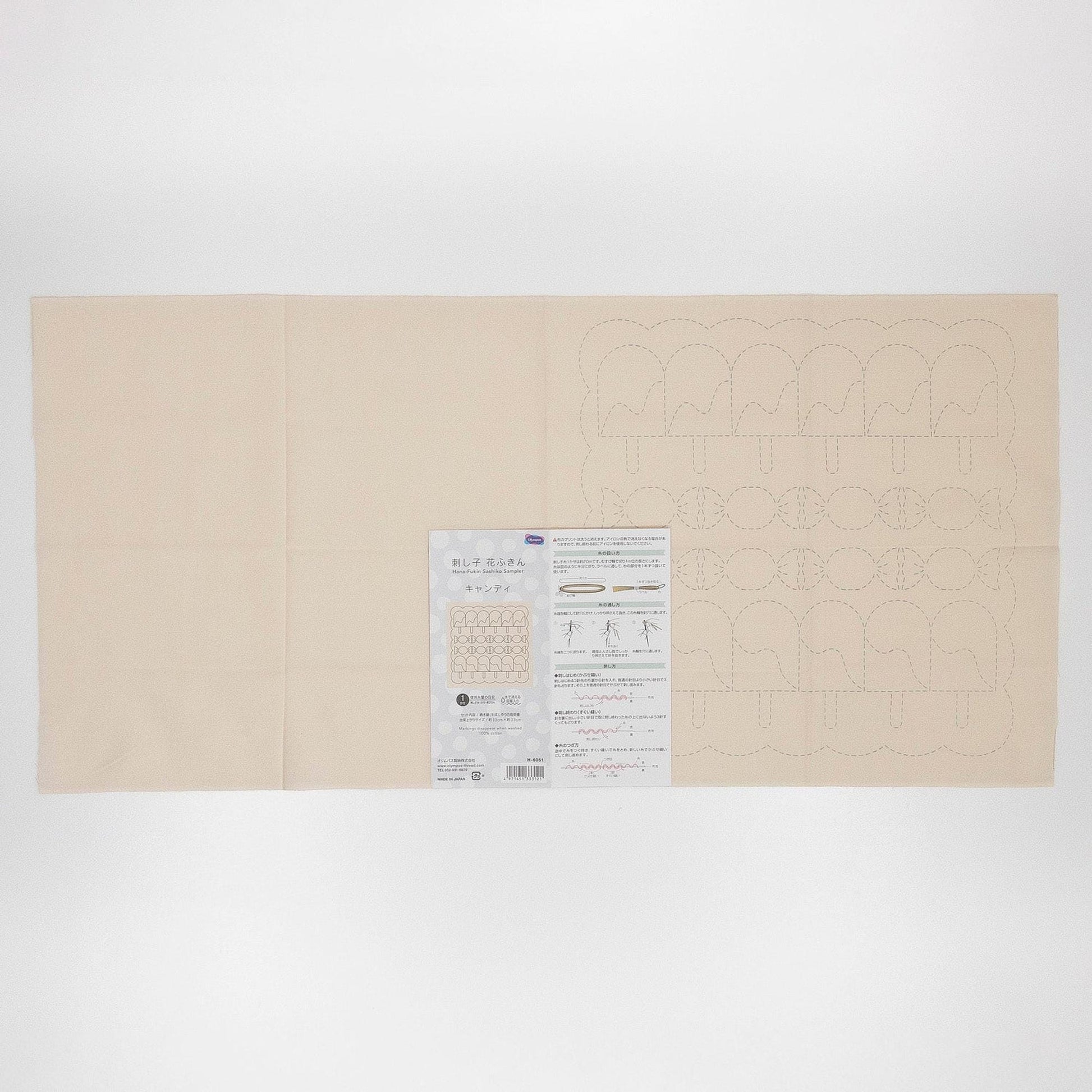 The image is a large, cream-colored fabric with a printed pattern on it. There is a small, white paper with text and diagrams next to the fabric.