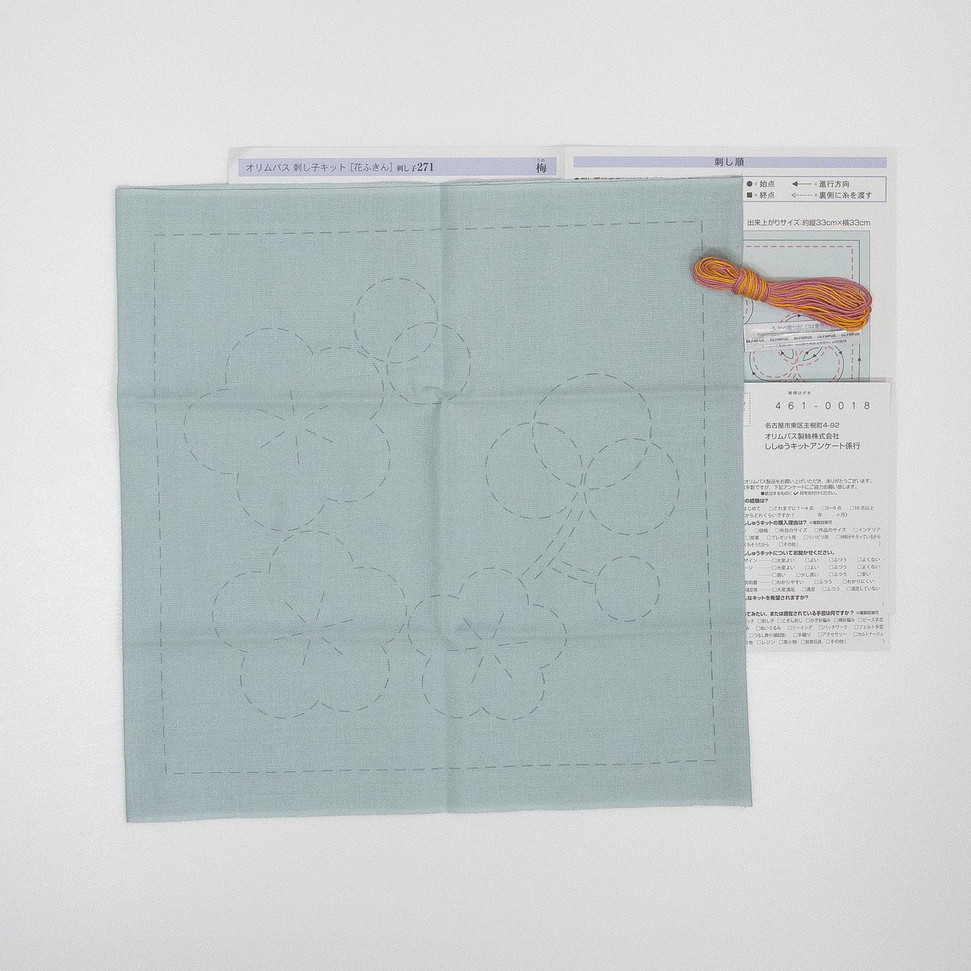 a light blue fabric with a flower design, along with some instructions or a diagram, and a small orange object, possibly a needle, placed on top of the fabric.