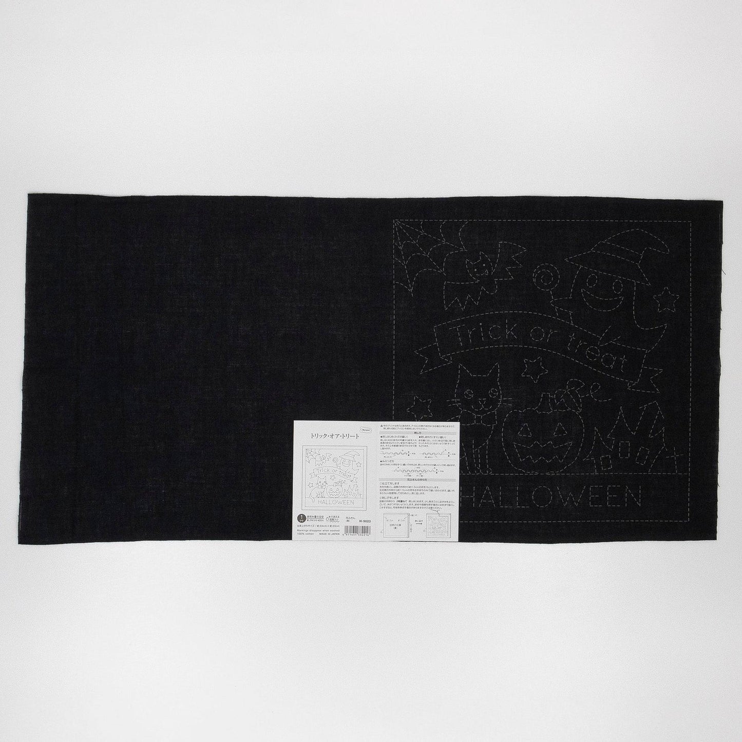 The image is a black and white photograph featuring a Halloween-themed quilt with a black background and a white label with Japanese text.