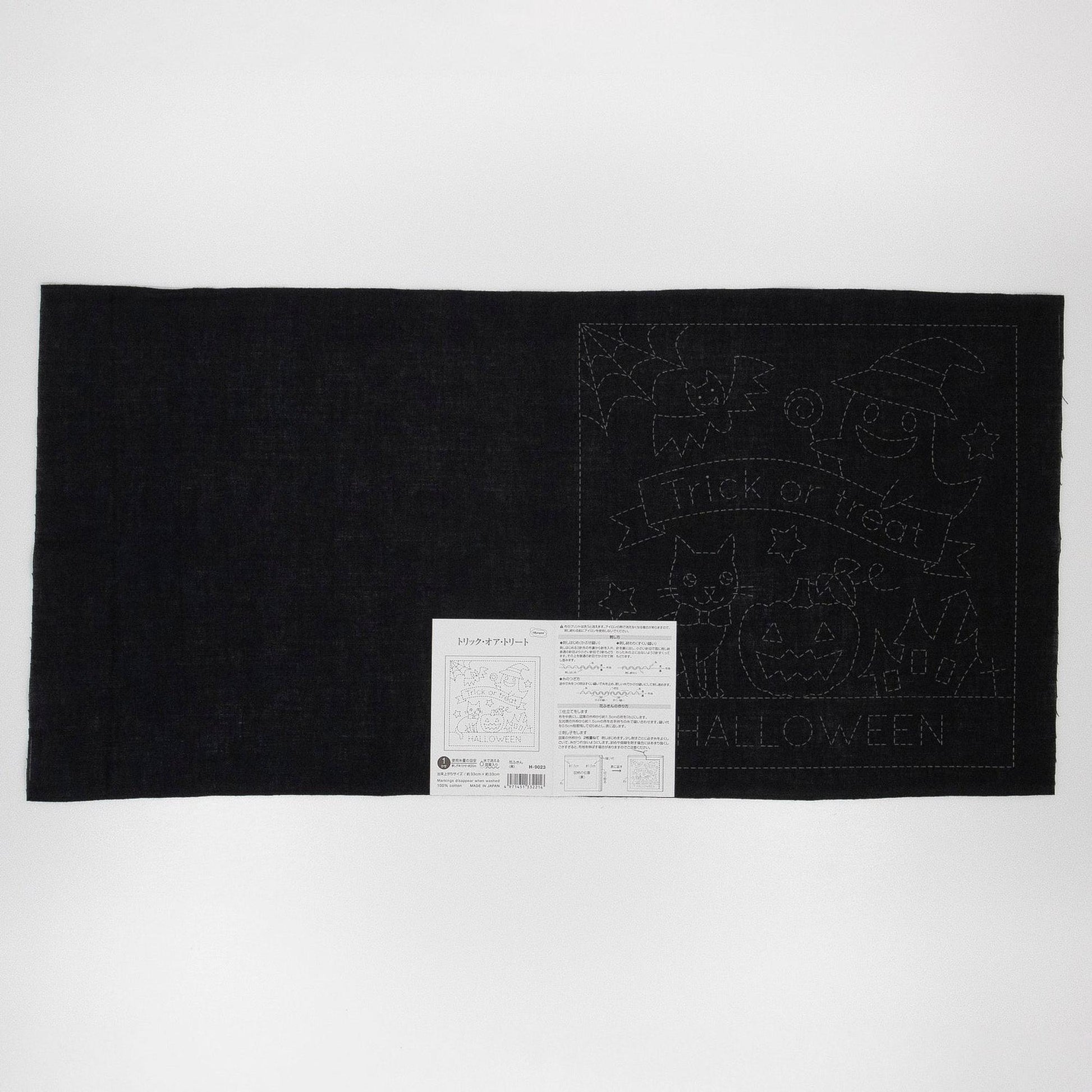 The image is a black and white photograph featuring a Halloween-themed quilt with a black background and a white label with Japanese text.