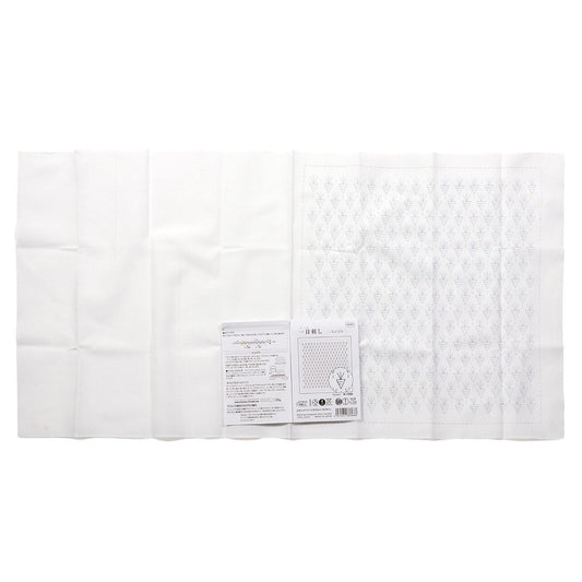 a white cloth with a patterned design, and there is a small booklet or pamphlet with text on it placed next to the cloth.