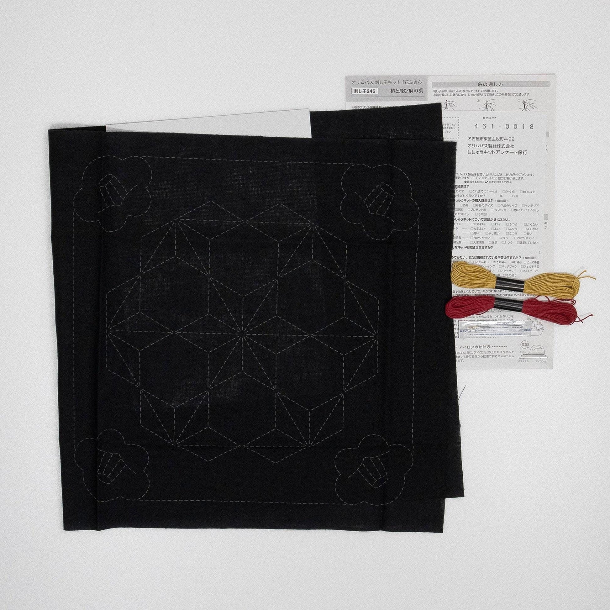 a black fabric with a geometric pattern, along with some thread and a piece of paper with text in Japanese.