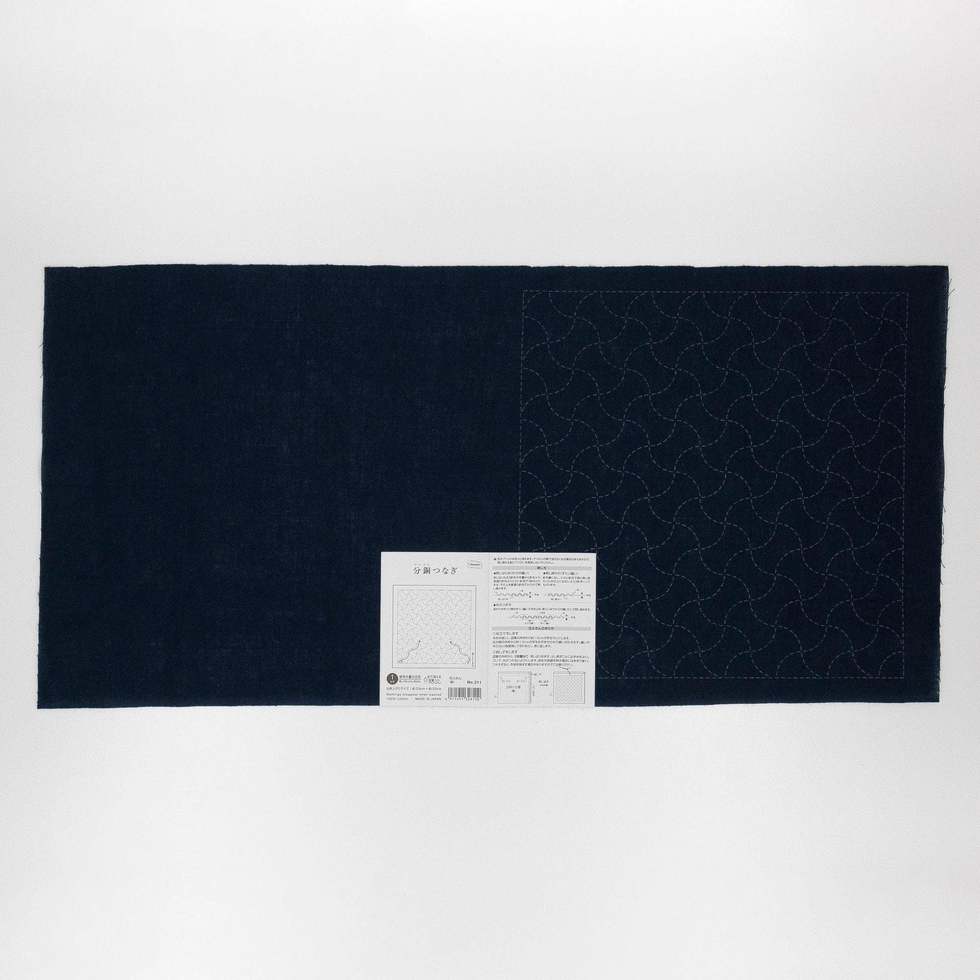 The image is a black and white photograph of a large piece of fabric with a pattern on it, accompanied by a small white label.