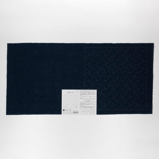 The image is a black and white photograph of a large piece of fabric with a pattern on it, accompanied by a small white label.
