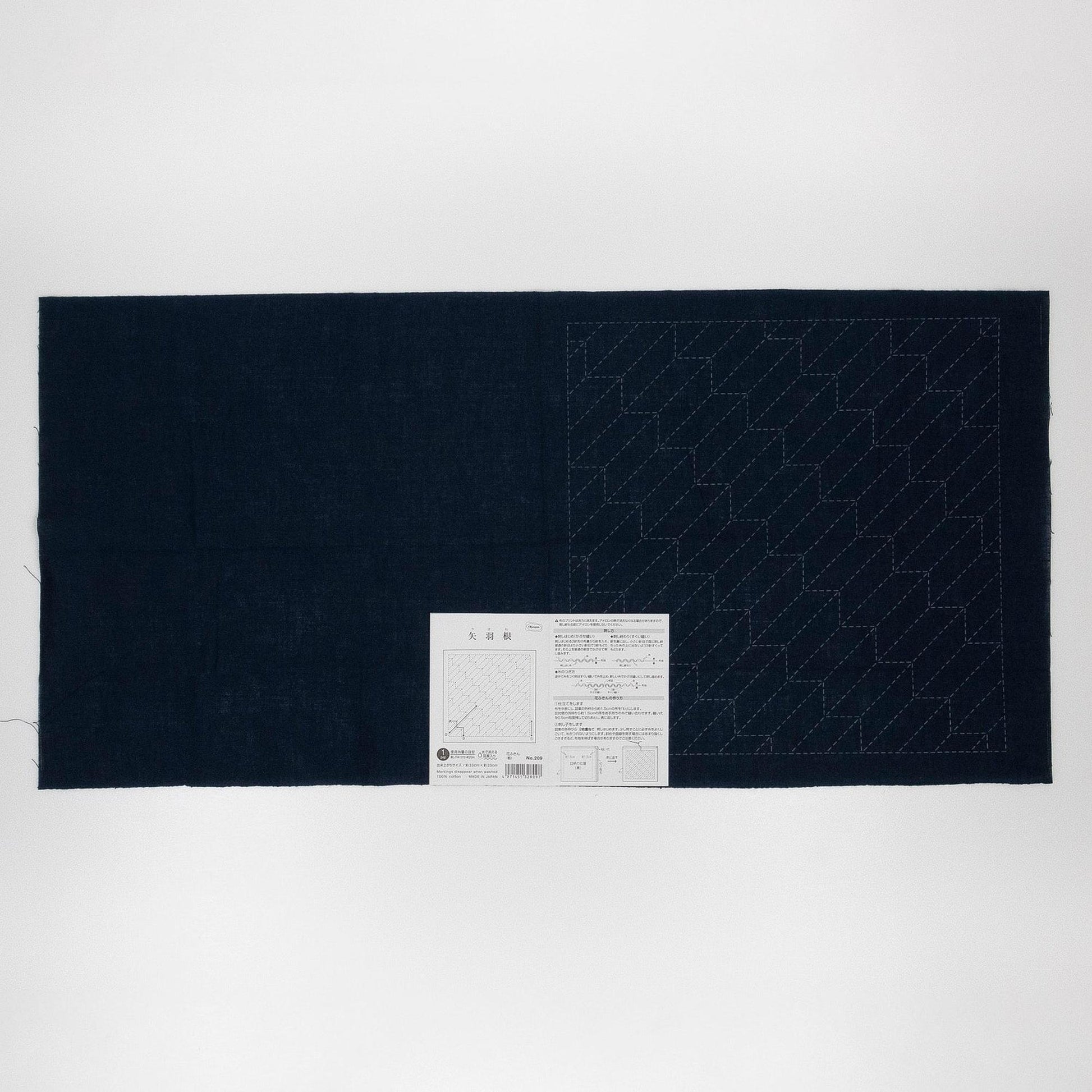 The image is a black and white photograph of a piece of fabric with a white paper attached to it, displaying a pattern or instructions.