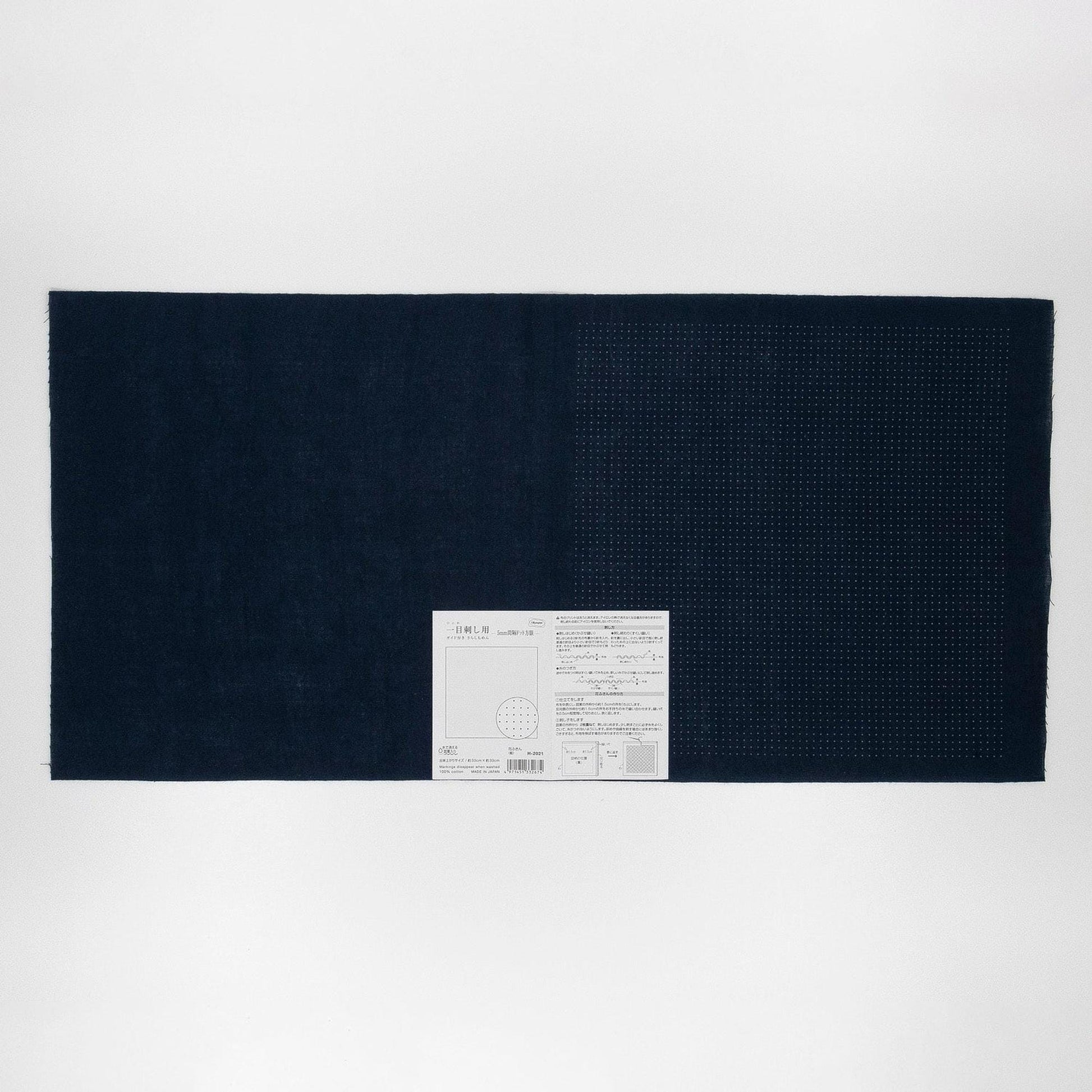 The image is a black and white photograph of a large rectangular piece of fabric or material, with a small white label or tag attached to it.