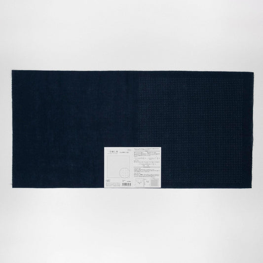 The image is a black and white photograph of a large rectangular piece of fabric or material, with a small white label or tag attached to it.