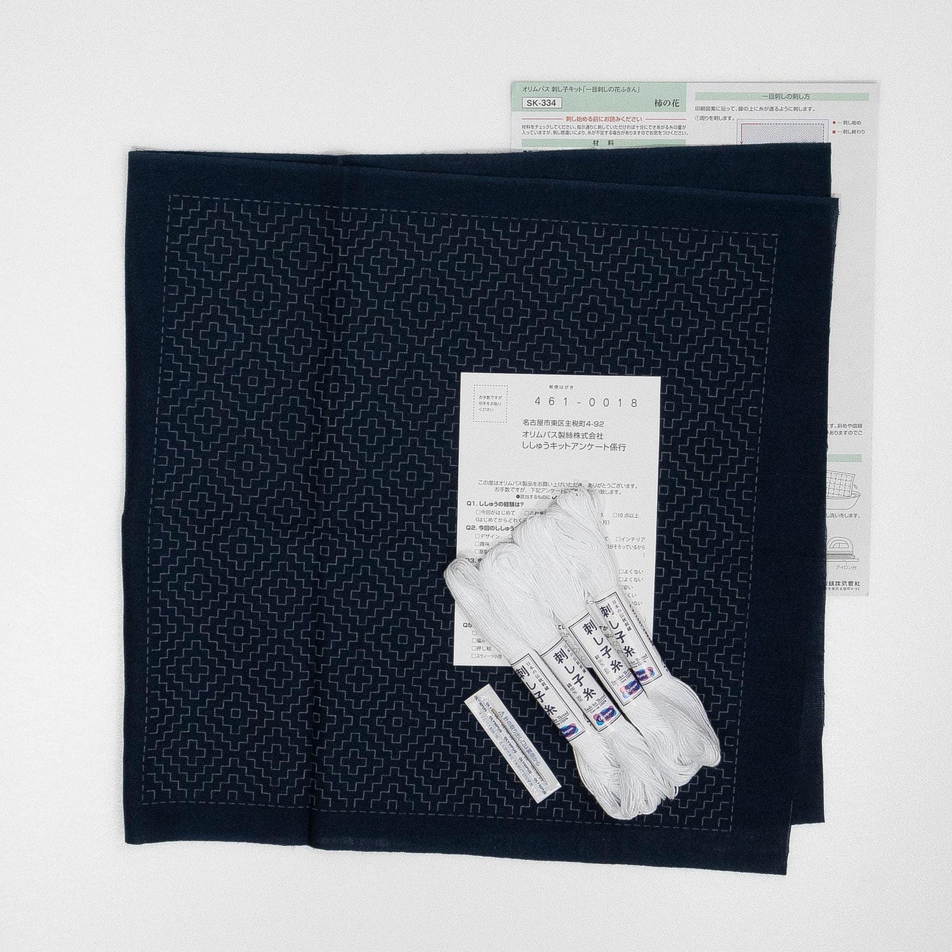 a black fabric with a geometric pattern, along with some white thread and a piece of paper with text in Japanese.
