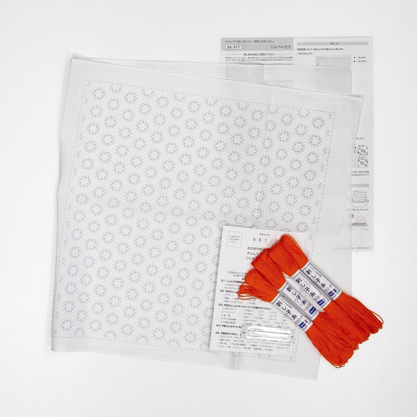 a sewing kit with a white square pattern, a set of orange thread, and some instructions or labels.