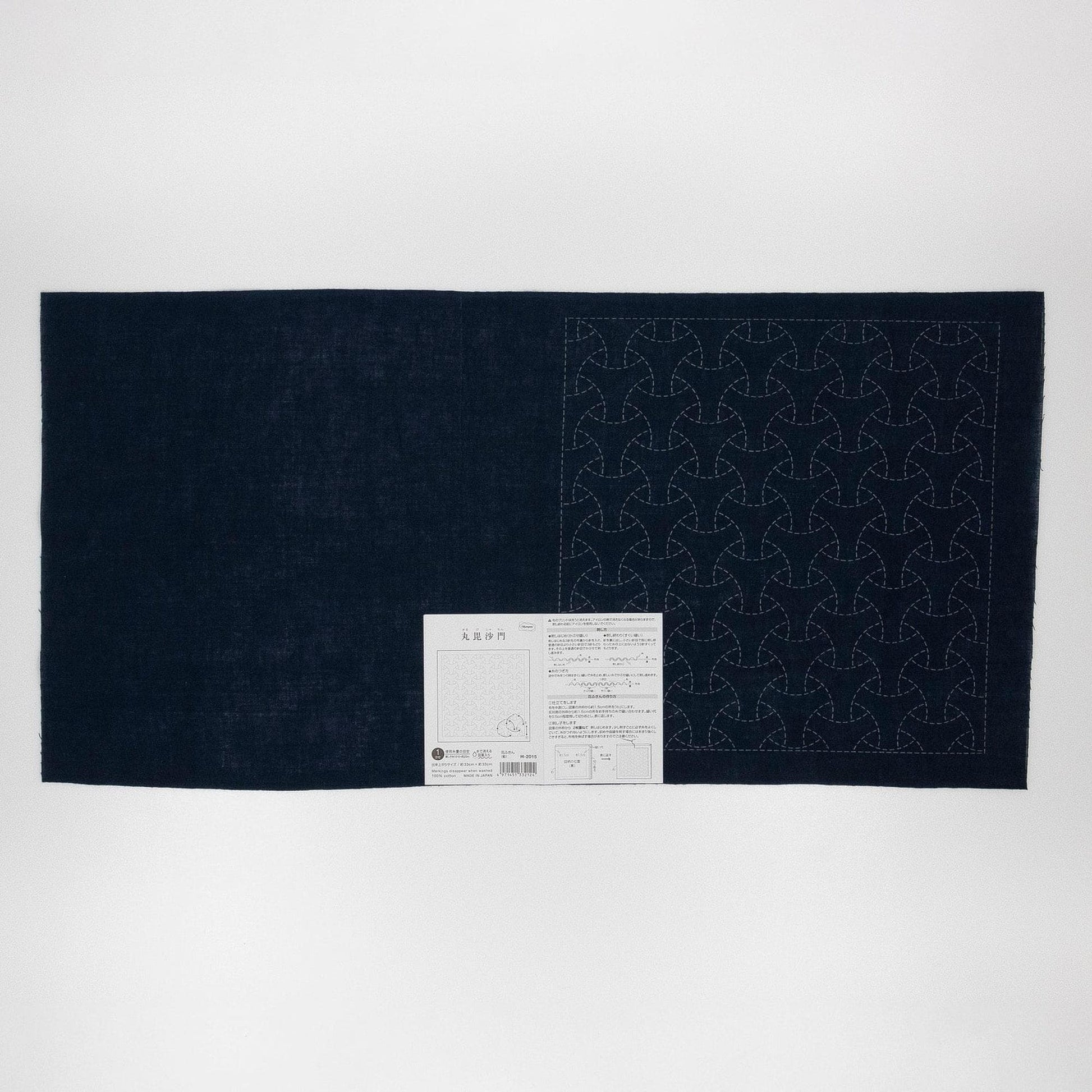 a dark fabric with a repeating pattern of circles or triangles, and there is a small white label or instruction sheet attached to the fabric.