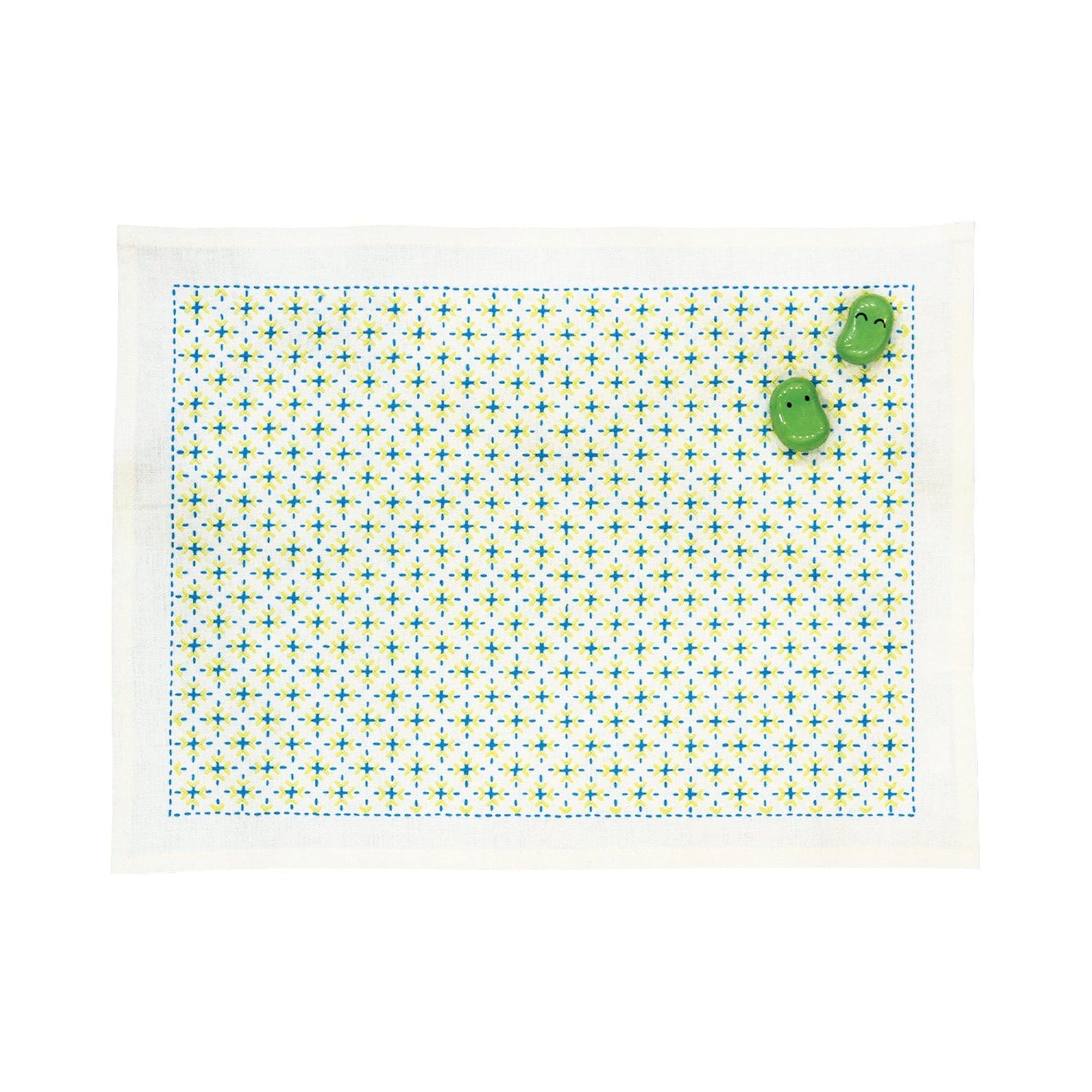 a white placemat with a green and white geometric pattern, and two green frog-shaped objects are placed on top of it.