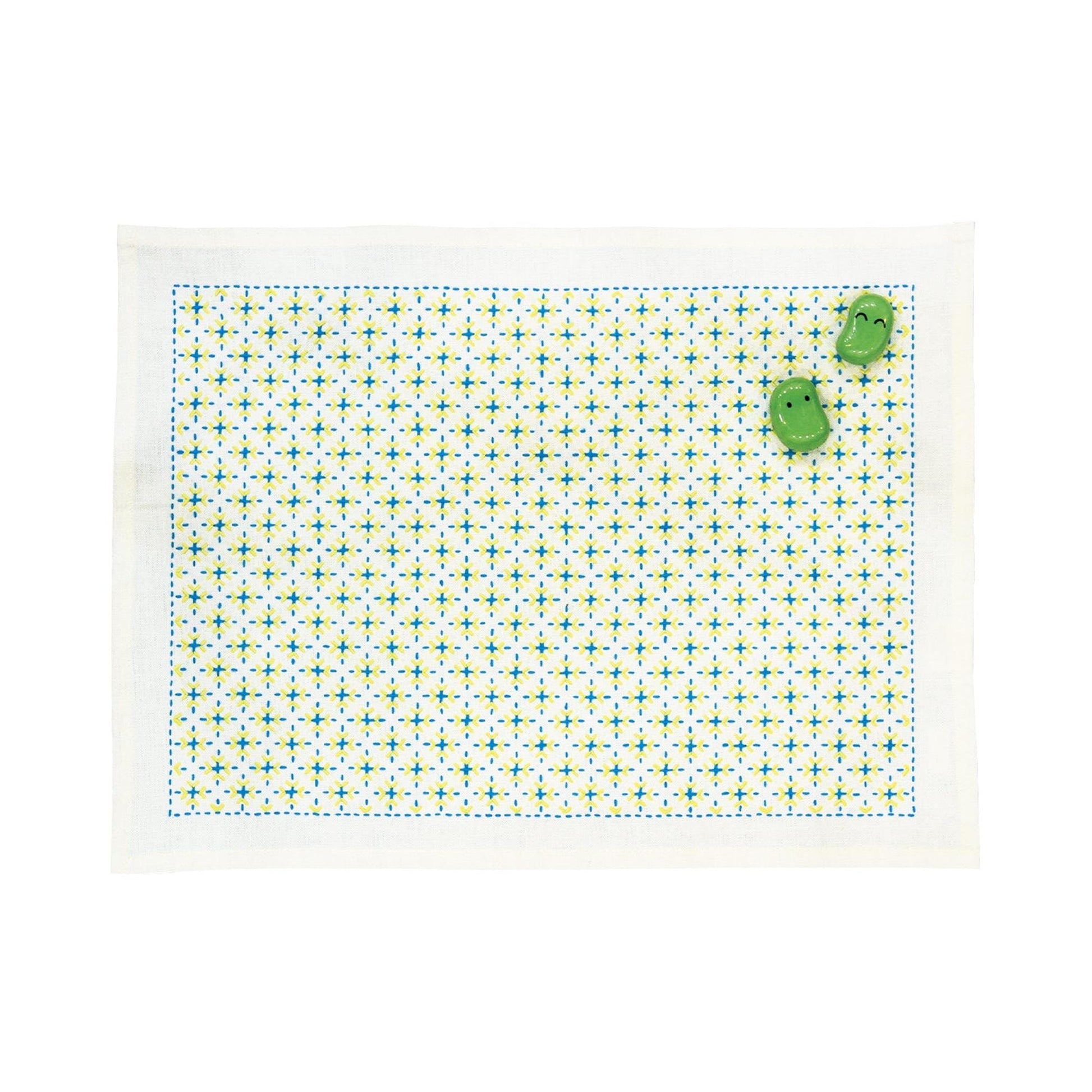 a white placemat with a green and white geometric pattern, and two green frog-shaped objects are placed on top of it.