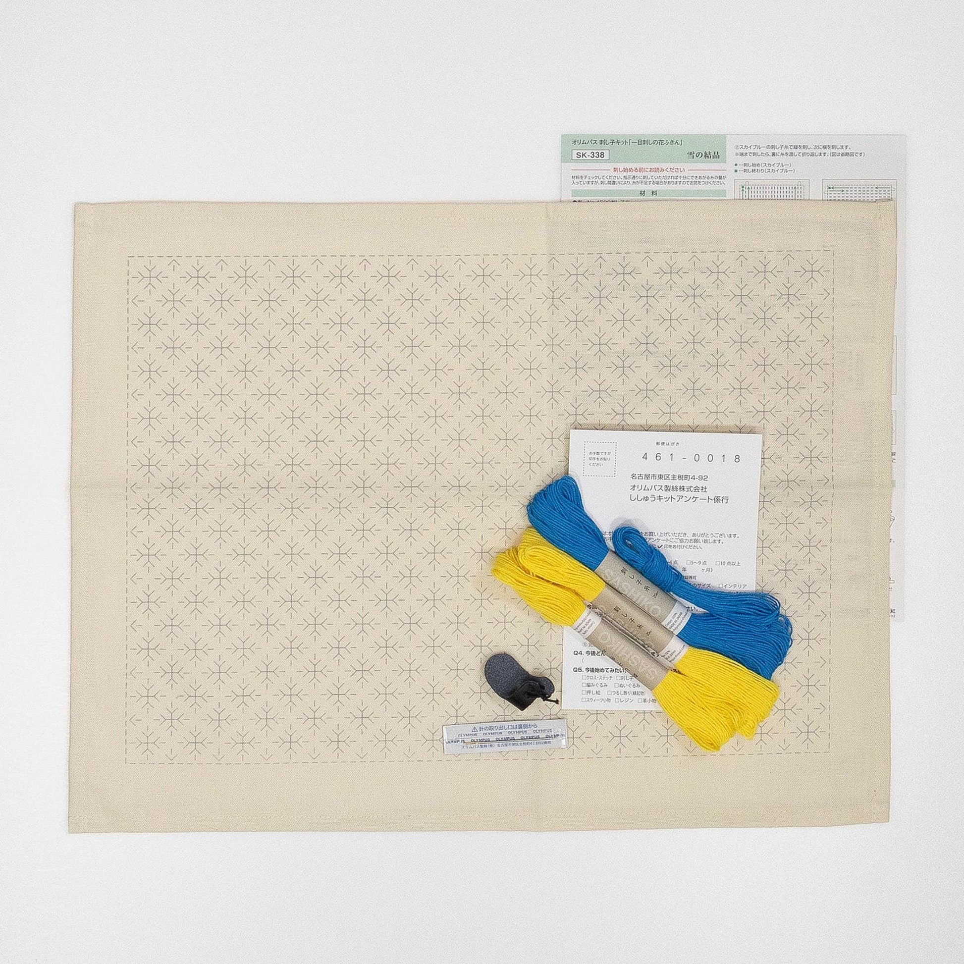 a beige fabric with a repeating star pattern, a pair of blue and yellow embroidery floss, and a small black object.
