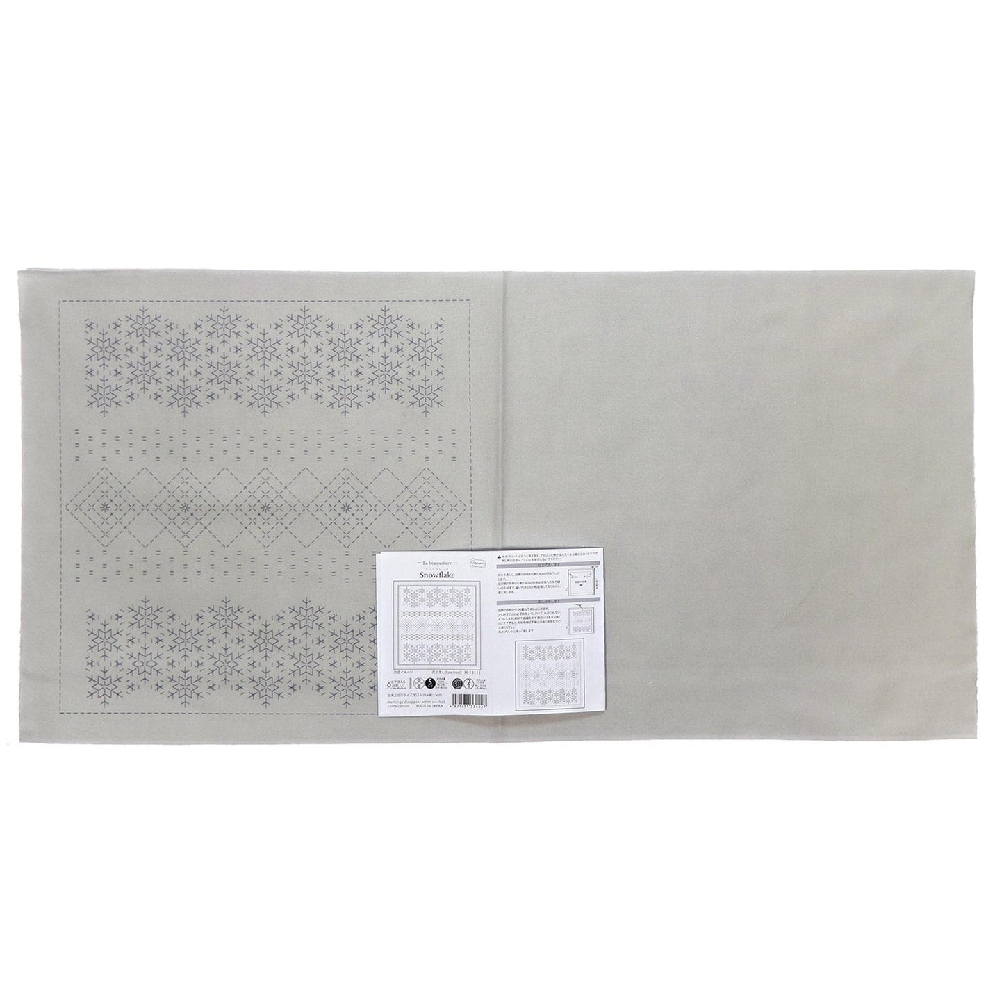 The image is a gray fabric with a repeating pattern of snowflakes on it. There is a white paper with text and a barcode attached to the fabric.