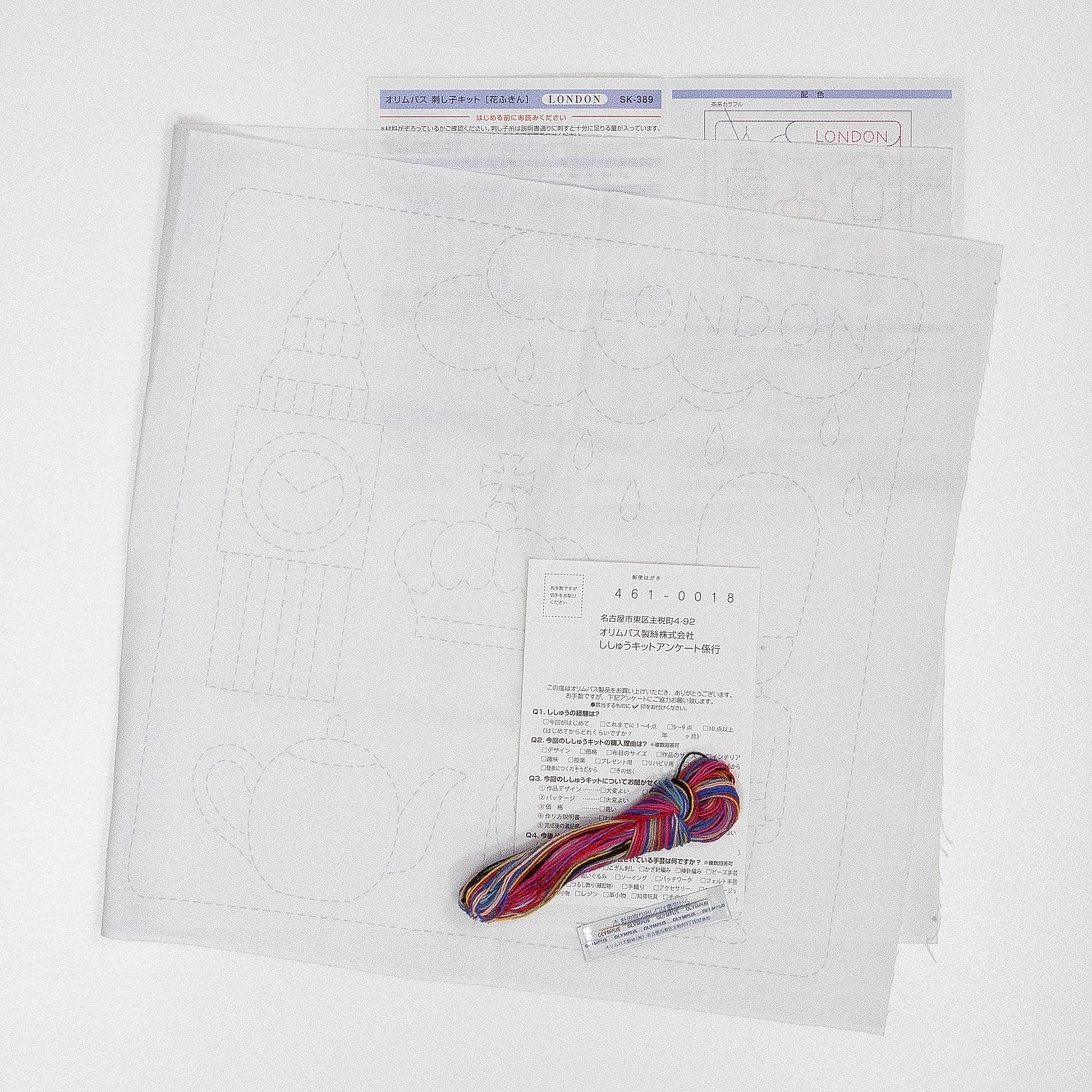 a piece of paper with a drawing of a city, a piece of paper with instructions, and a spool of thread and a needle, all placed on a white background.