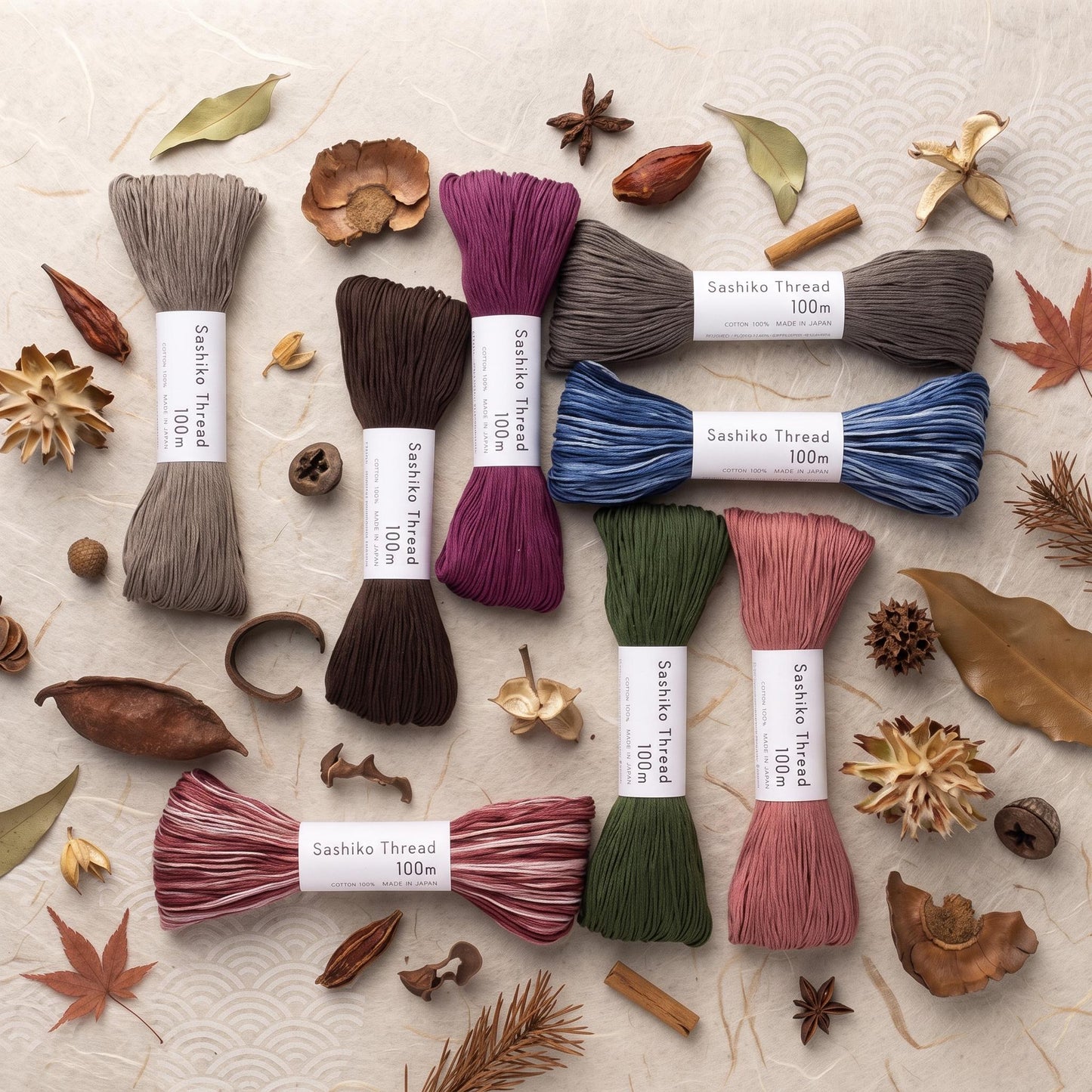 various types of thread, including silk, cotton, and jute, arranged on a surface with dried leaves, pine cones, and other natural elements.