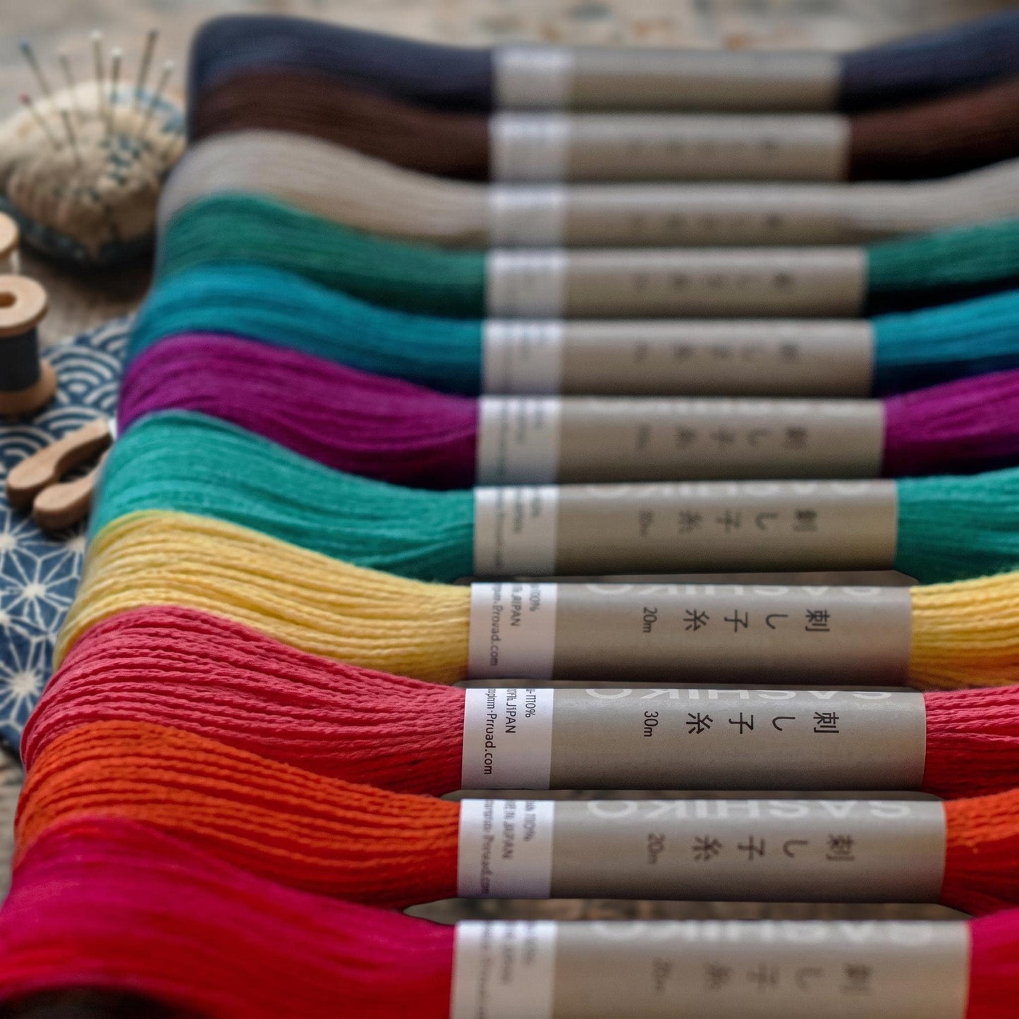 A collection of colorful spools of thread arranged in a row, with labels indicating the type of thread and the size in centimeters.