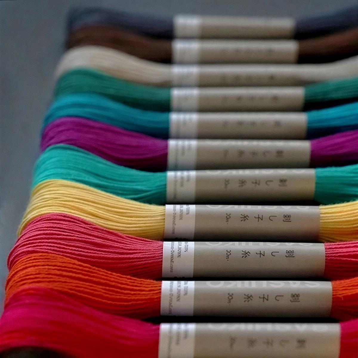 A collection of colorful spools of thread or yarn, each with a label in a foreign language, arranged in a row.