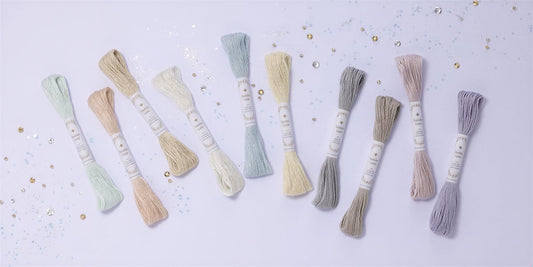 A collection of various colored spools of thread arranged on a light purple background, with scattered glitter around them.