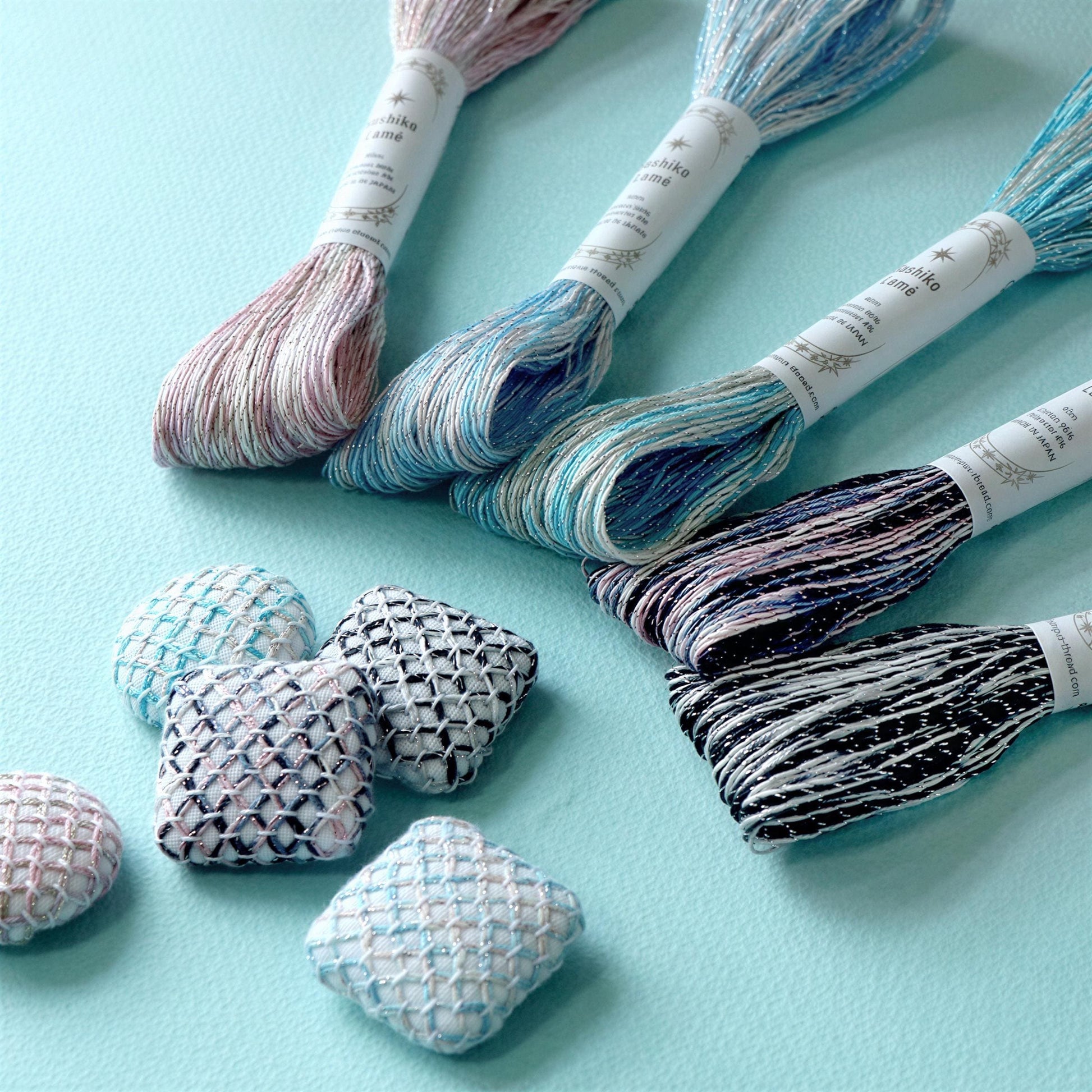 a collection of colorful spools of thread and small woven objects, including squares and small balls, arranged on a light blue background.