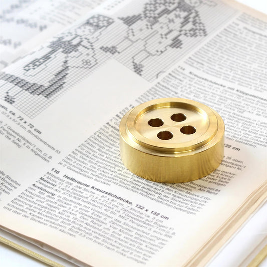 a close-up of a book with a cross-stitch pattern on the page, and a brass button placed on top of the page.
