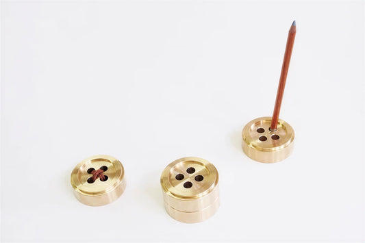 three brass pencil holders, each with a single pencil inserted, and a single red pencil standing upright in one of the holders.