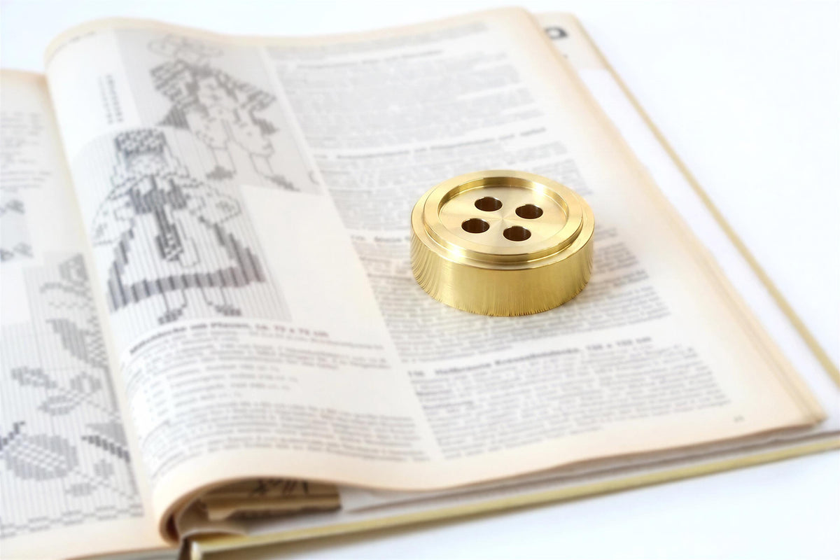 an open book with a gold-colored metal object, likely a button, placed on top of the pages.