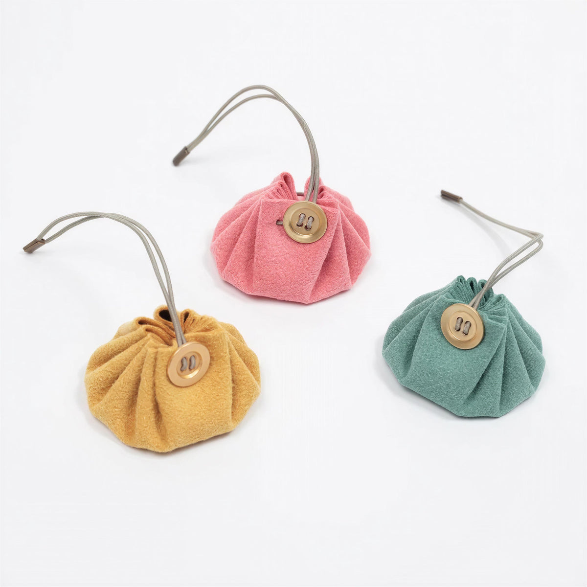 Three small, colorful fabric pouches or bags with metal buttons attached, arranged in a row on a white background.