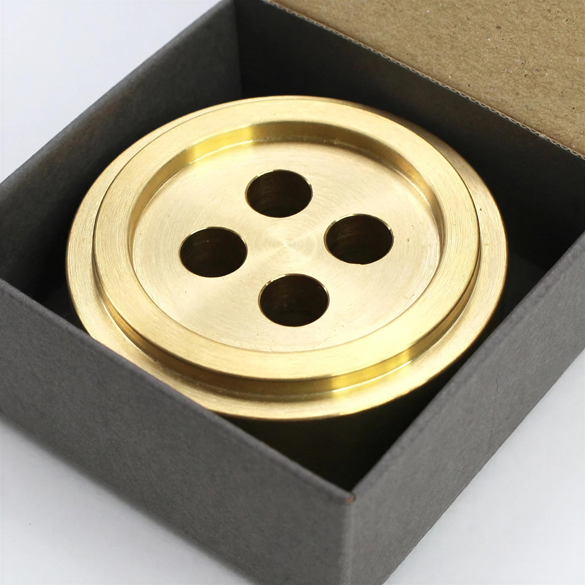 A brass button-like object is displayed in a black box.