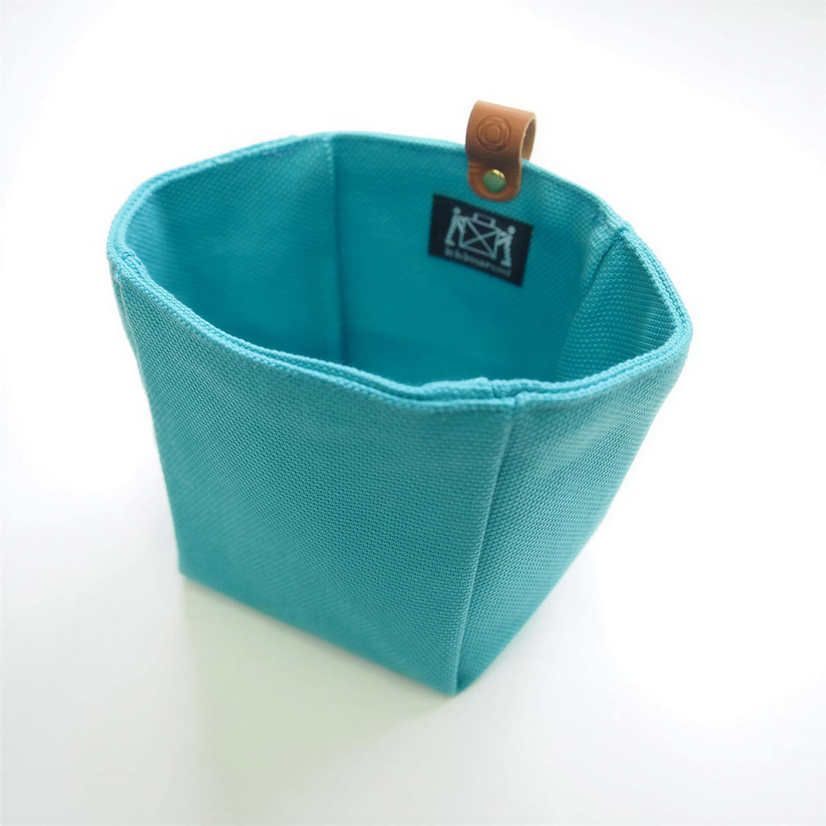 A turquoise-colored fabric basket with a leather tag attached to it.