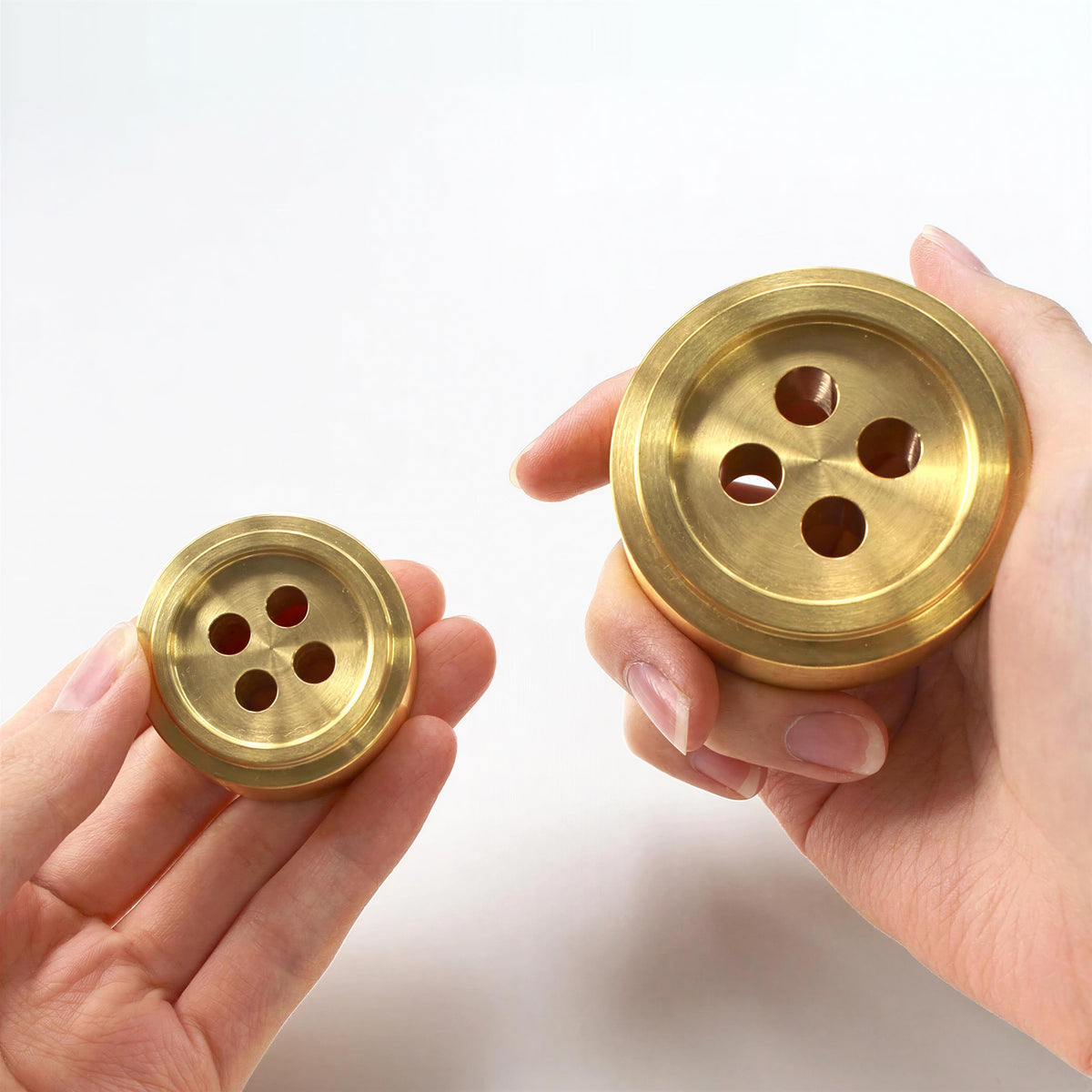 Two hands holding golden-colored metal objects resembling buttons.