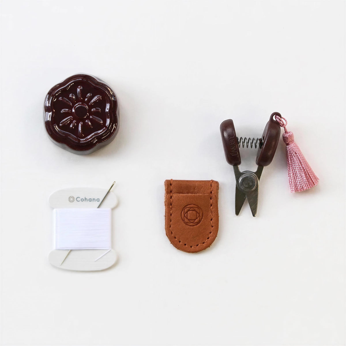 various craft supplies, including a pair of scissors, a tassel, a spool of thread, and a small leather pouch.