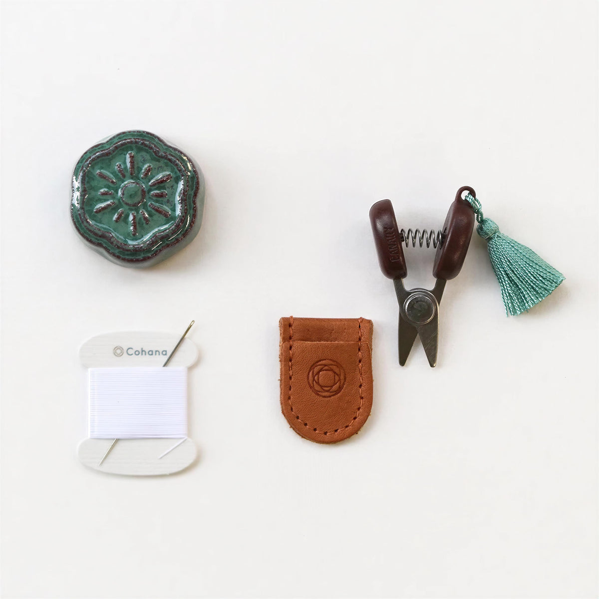 various craft supplies, including a green ceramic object, a pair of brown scissors, a spool of thread, a leather pouch, and a tassel.