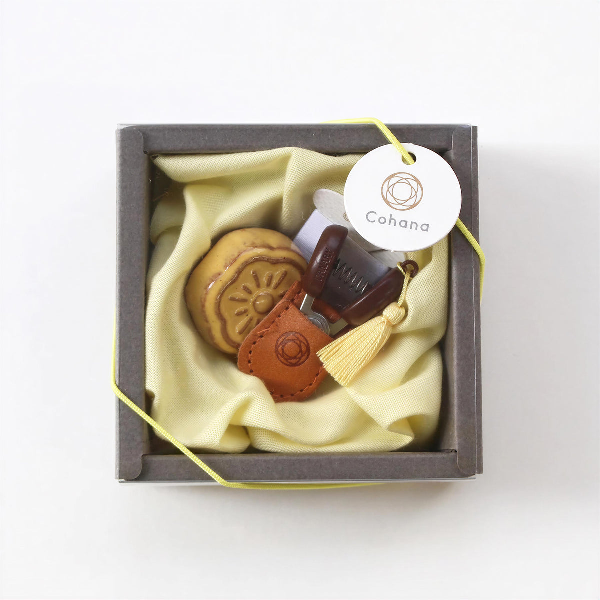 A small, square-shaped box containing a yellow cloth, a brown leather keychain, and a small round object.