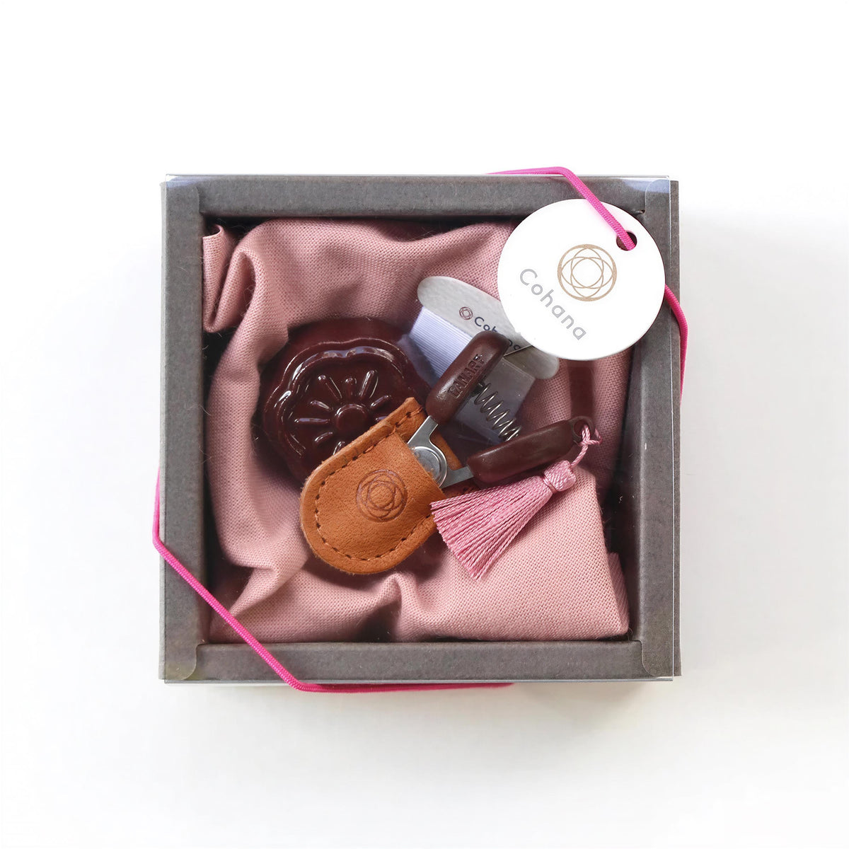 A small, square box containing a pink cloth, a brown leather item, and a white tag with a logo.