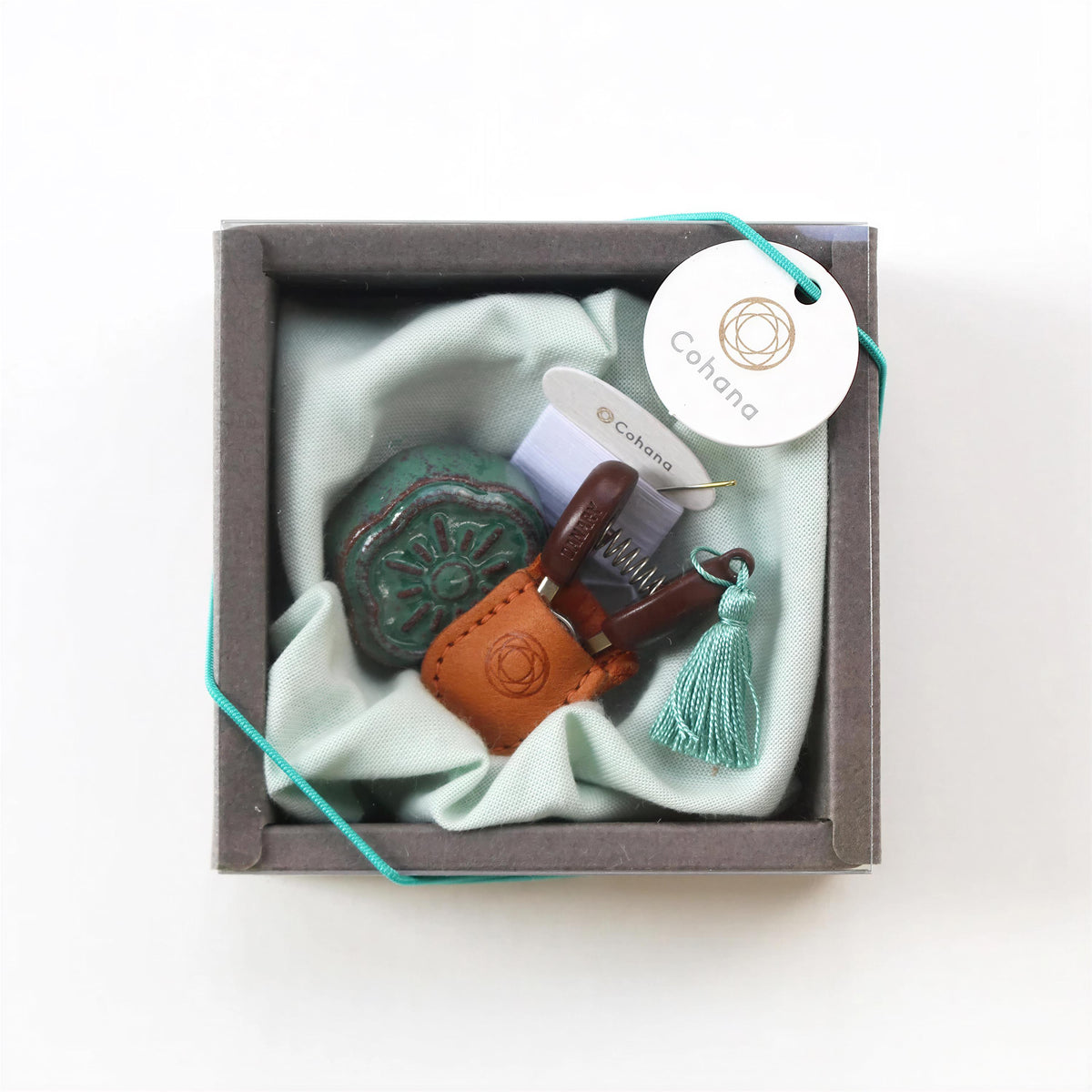 A small, square-shaped box containing a variety of items, including a green ceramic object, a brown leather item, and a tassel.
