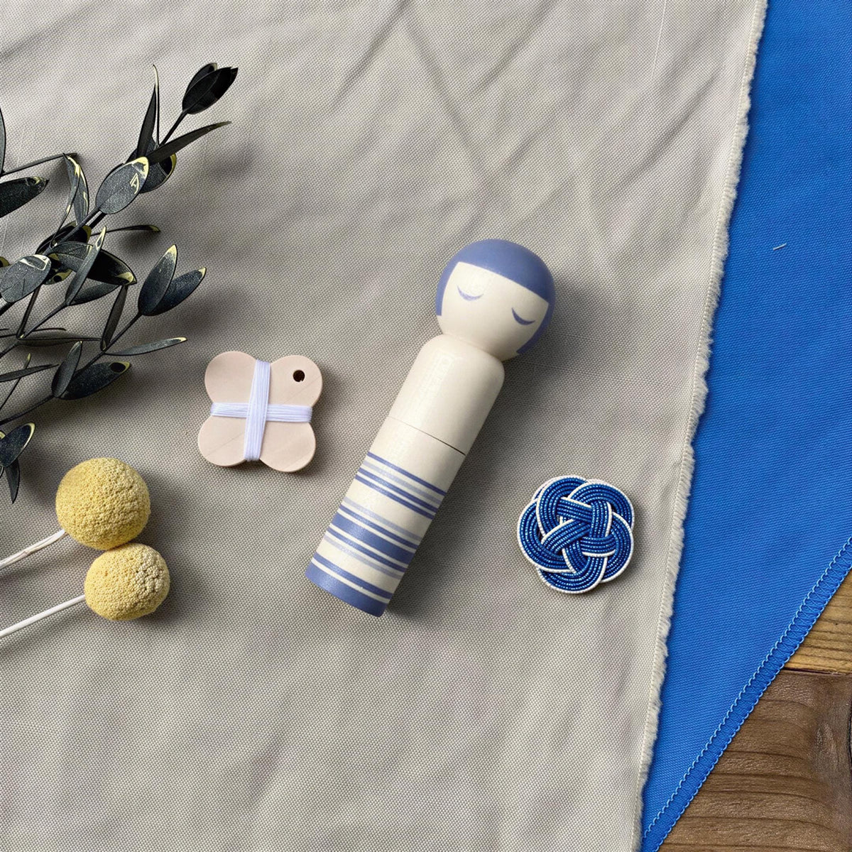 a wooden doll with blue and white stripes, a small wooden butterfly, and a blue and white button on a grey cloth.