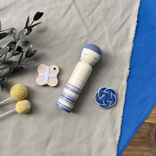 a wooden doll with blue and white stripes, a small wooden butterfly, and a blue and white button on a grey cloth.