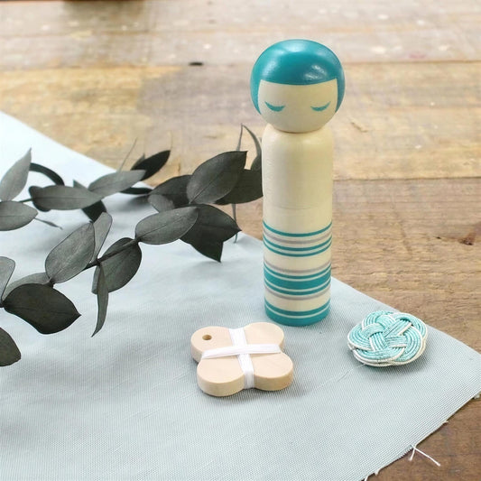 a wooden doll with a blue head, a small wooden butterfly, and a small wooden button, all placed on a light blue cloth.