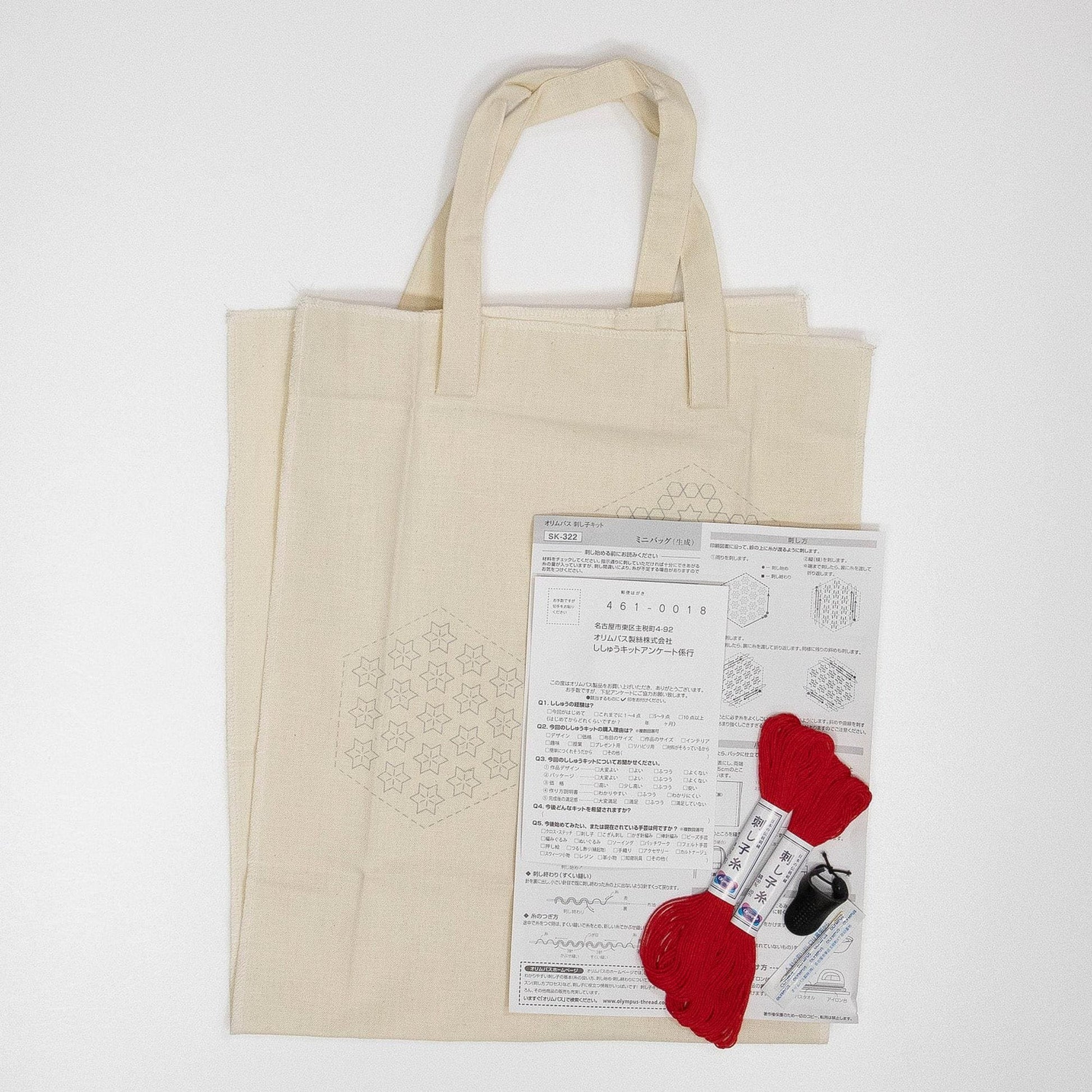 a beige tote bag with a patterned design, along with a set of instructions and materials, including a spool of red thread and a pair of scissors.