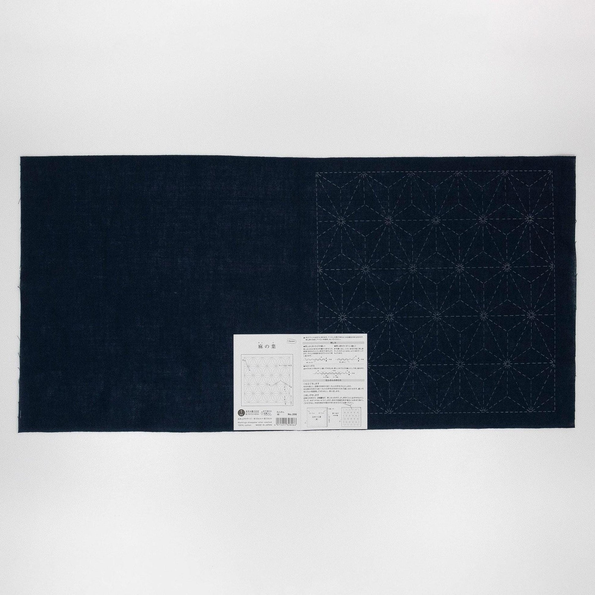 a dark blue fabric with a white pattern on it, and there is a small white label or instructions next to it.