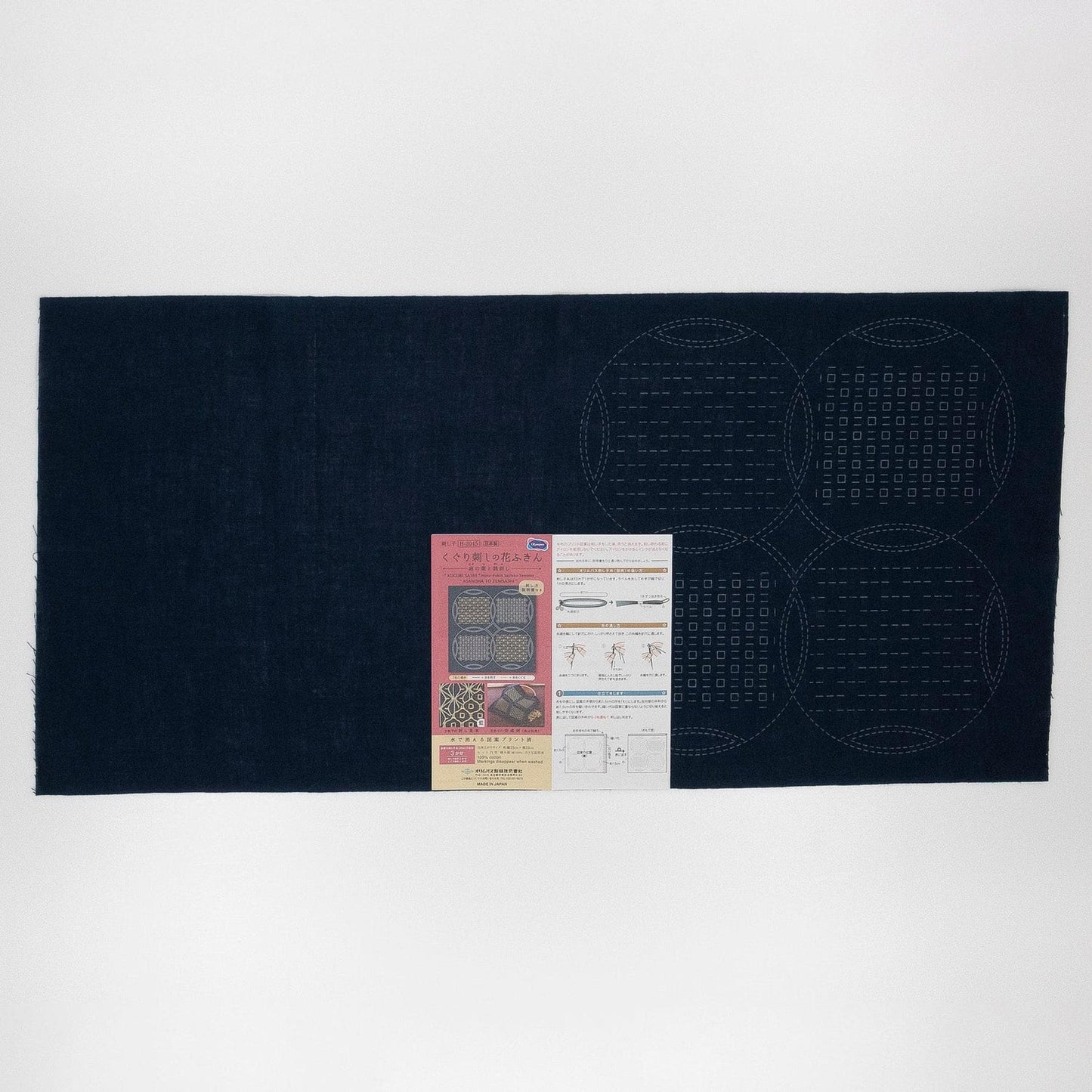 The image is a dark blue fabric with a pattern of circles on it, and there is a small piece of paper with text and images attached to it.